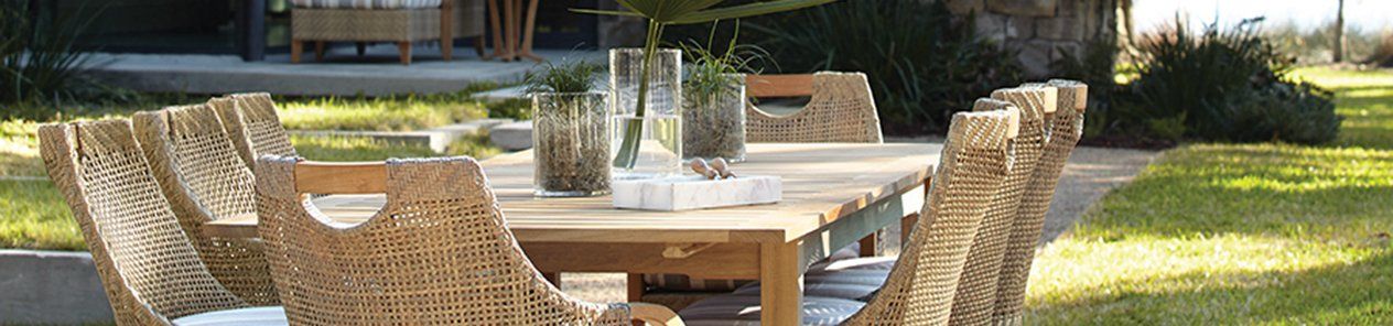 A long wooden table with wicker chairs in a backyard.