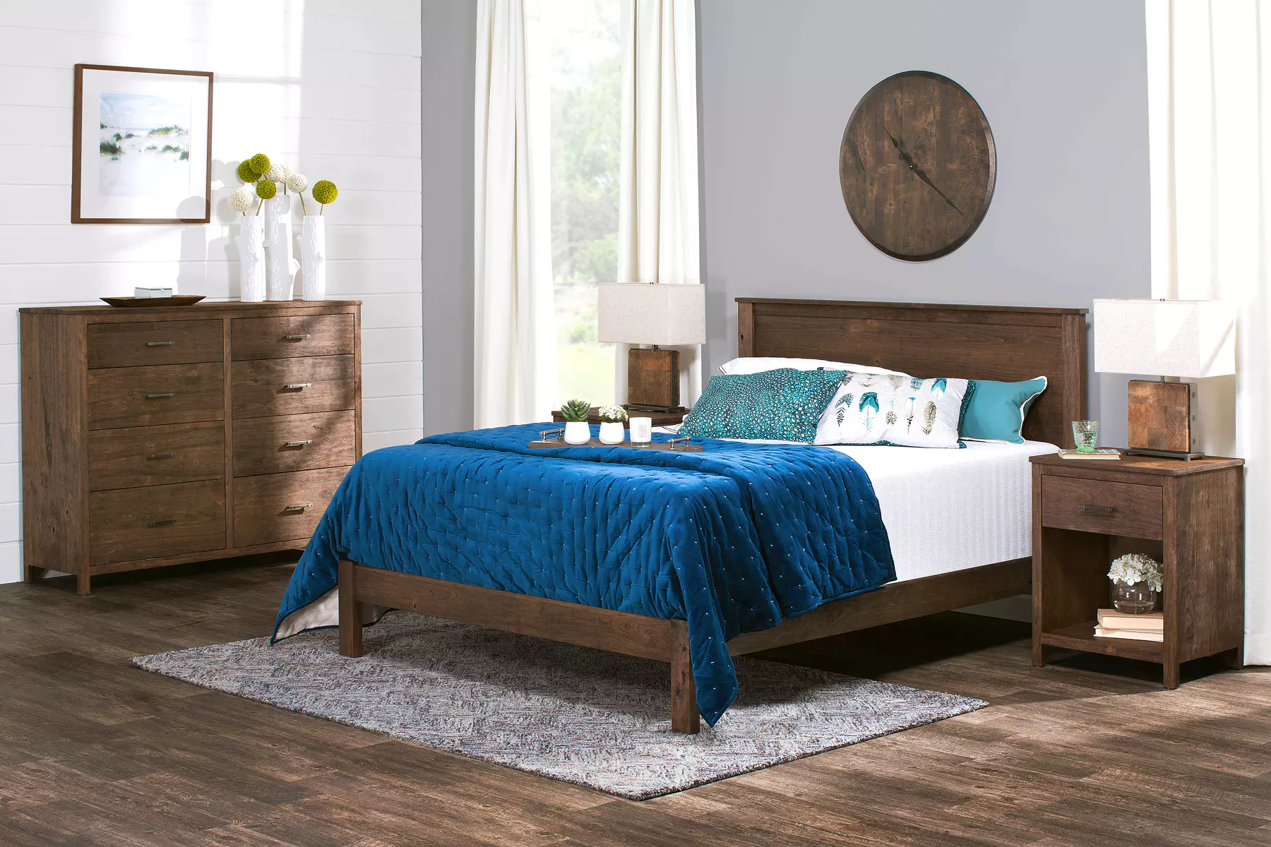 A bedroom with a bed , nightstand , dresser and a clock on the wall.