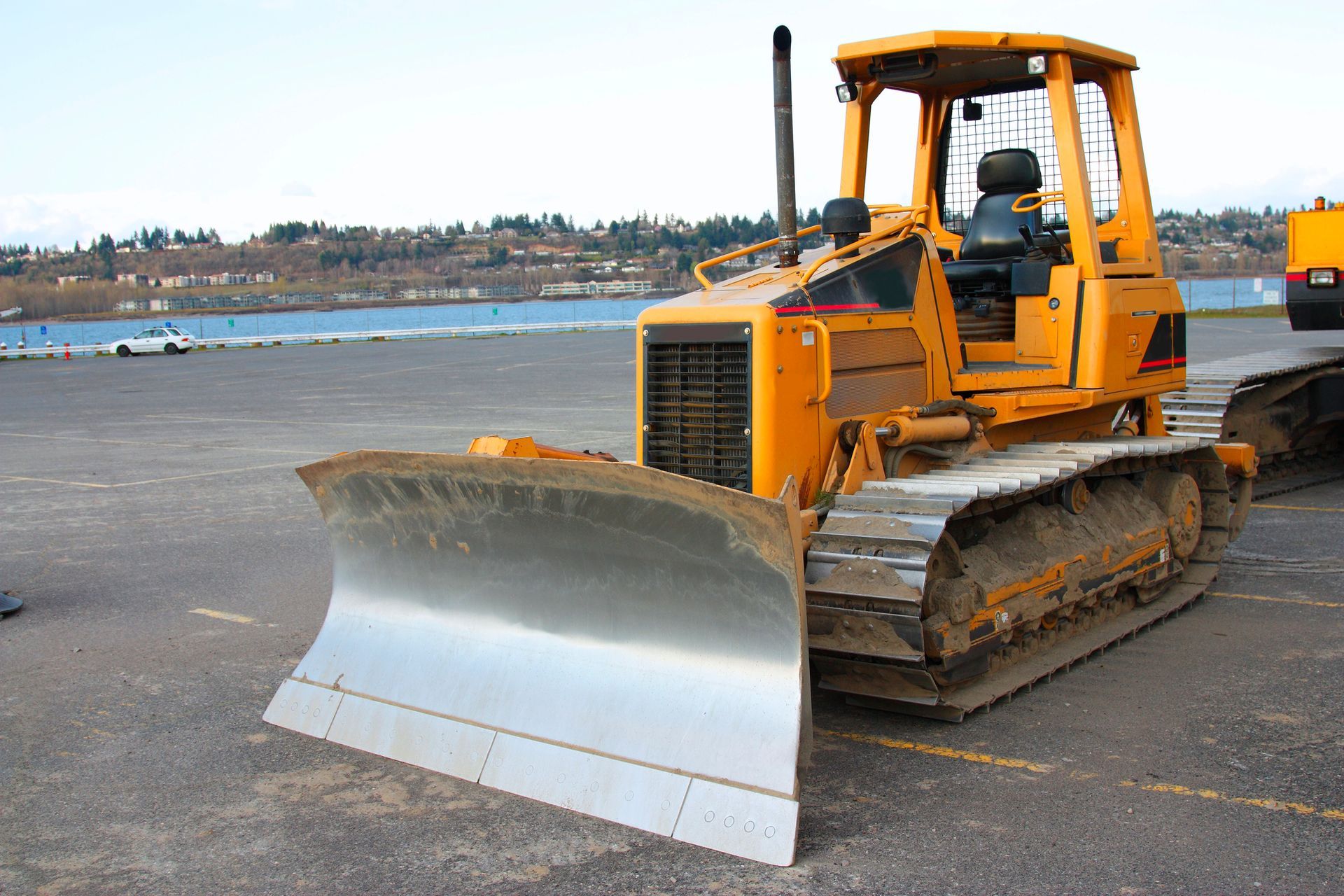 Una excavadora amarilla con una gran pala frontal está estacionada en el pavimento cerca de un muelle.