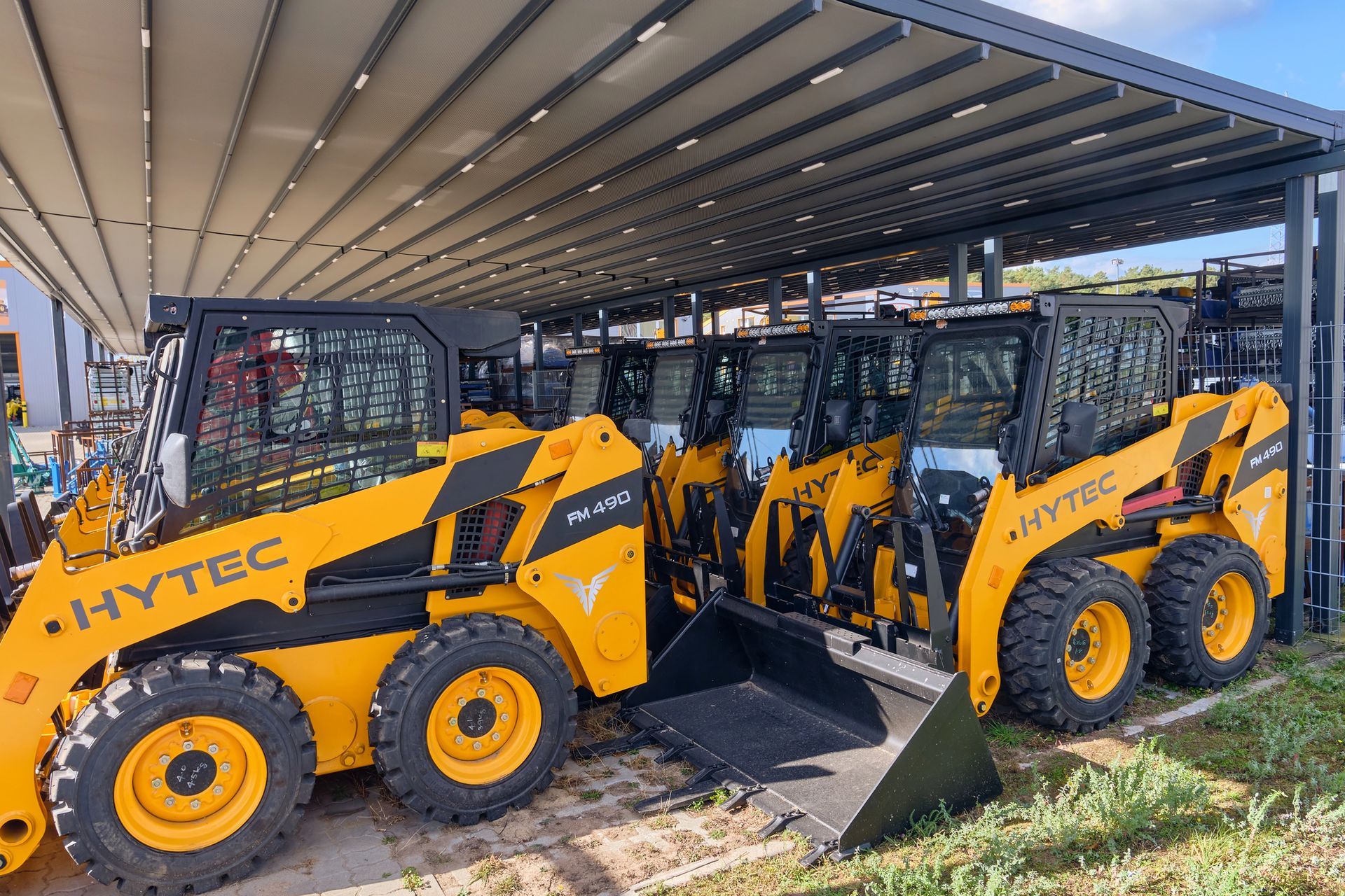 Cargadoras de construcción HYVTEC amarillas estacionadas bajo un cobertizo metálico.