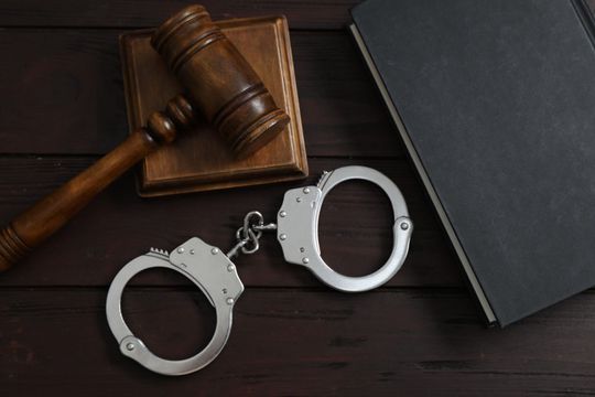 Handcuffs beside a judge’s gavel and closed black folder on a dark desk