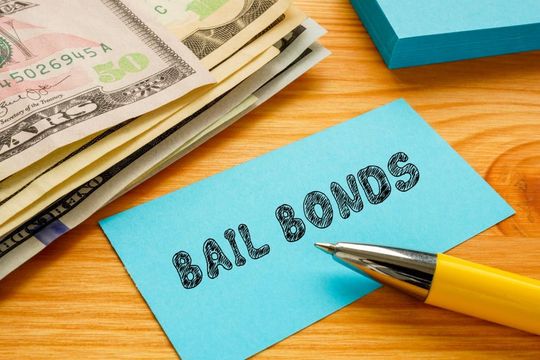Blue “Bail Bonds” card beside cash and a yellow pen on a wooden desk