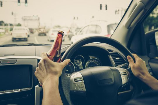 Hands on steering wheel while holding a beer bottle and driving in traffic