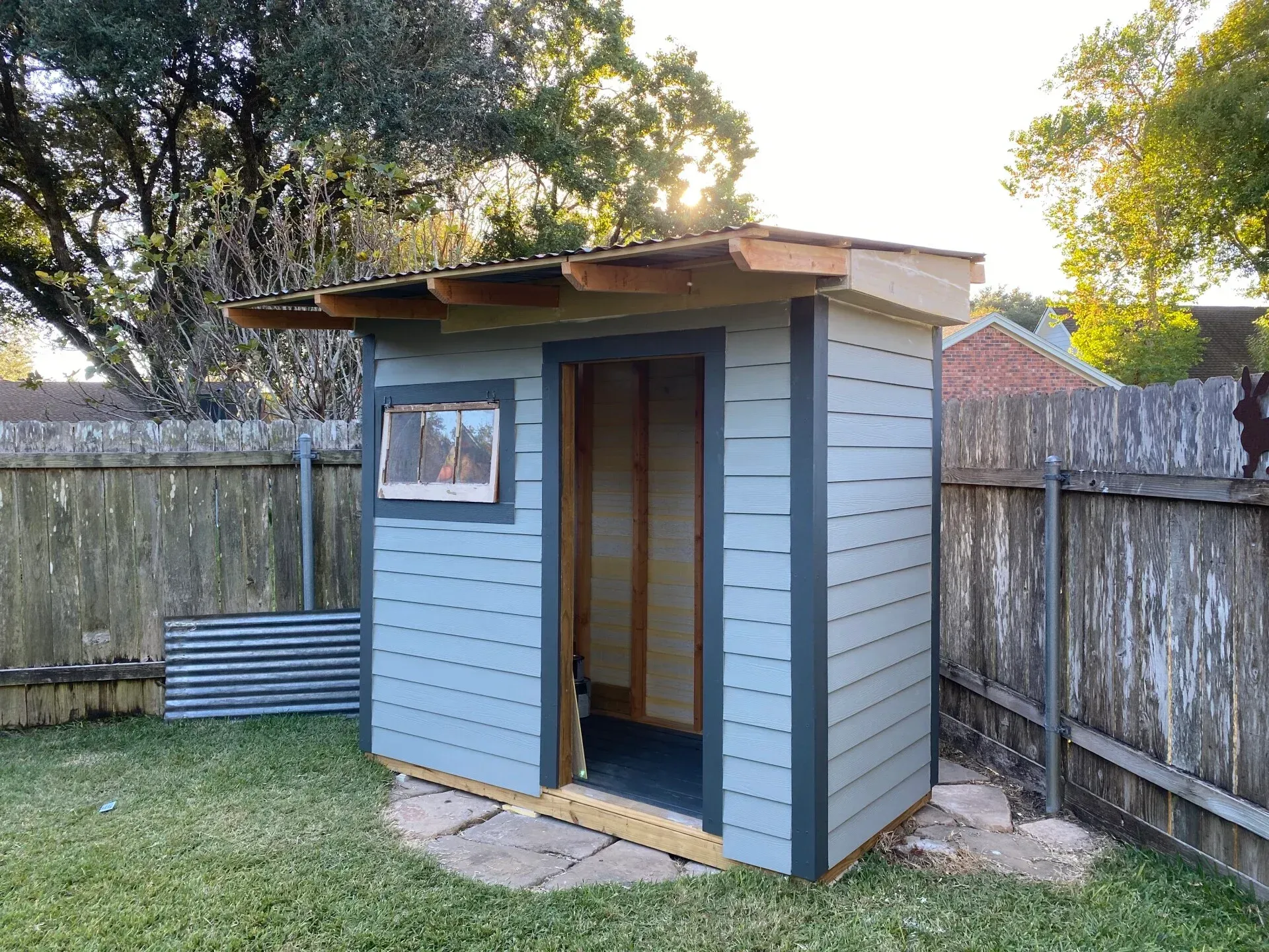 Small blue shed in backyard with open door and small window.