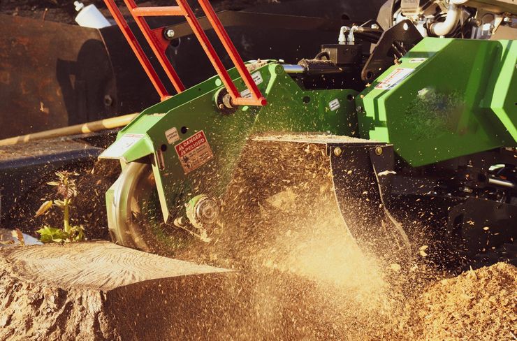 Green wood chipper throwing a spray of wood chips and dust