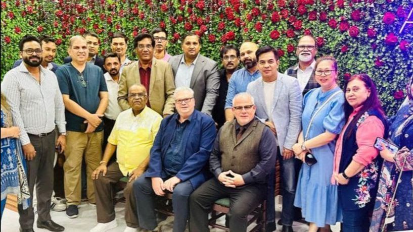 A group of people are posing for a picture in front of a wall of roses.