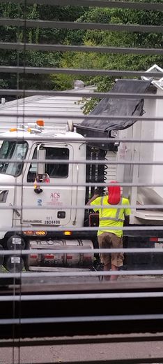 Utility truck with worker in neon vest unloading debris behind a fence.