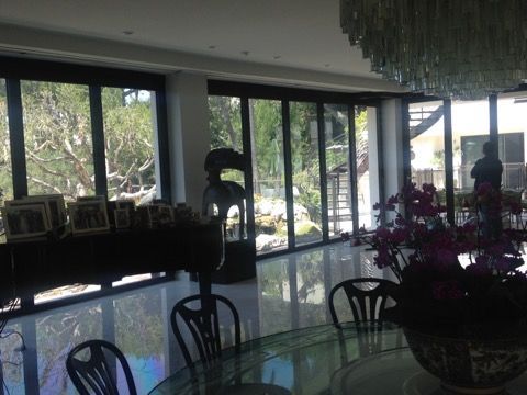 Interior dining area with large windows overlooking a garden. Black chairs surround a table. A person stands near a window.