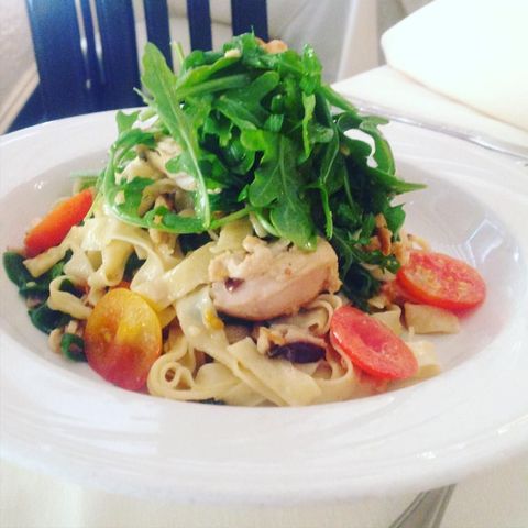 A bowl of pasta with tomatoes and greens on top