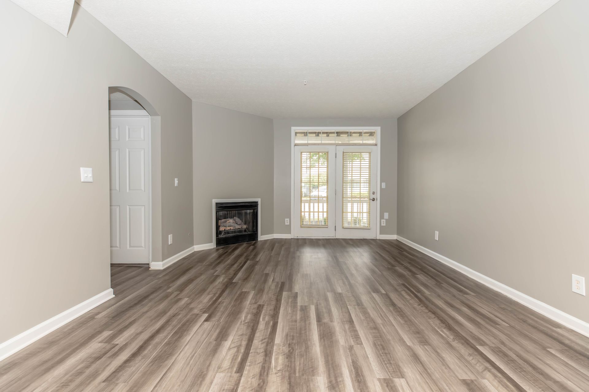 Empty living room with gray walls, wood-look flooring, fireplace, and French doors at Quarry Apartments for Rent in Columbus, OH.