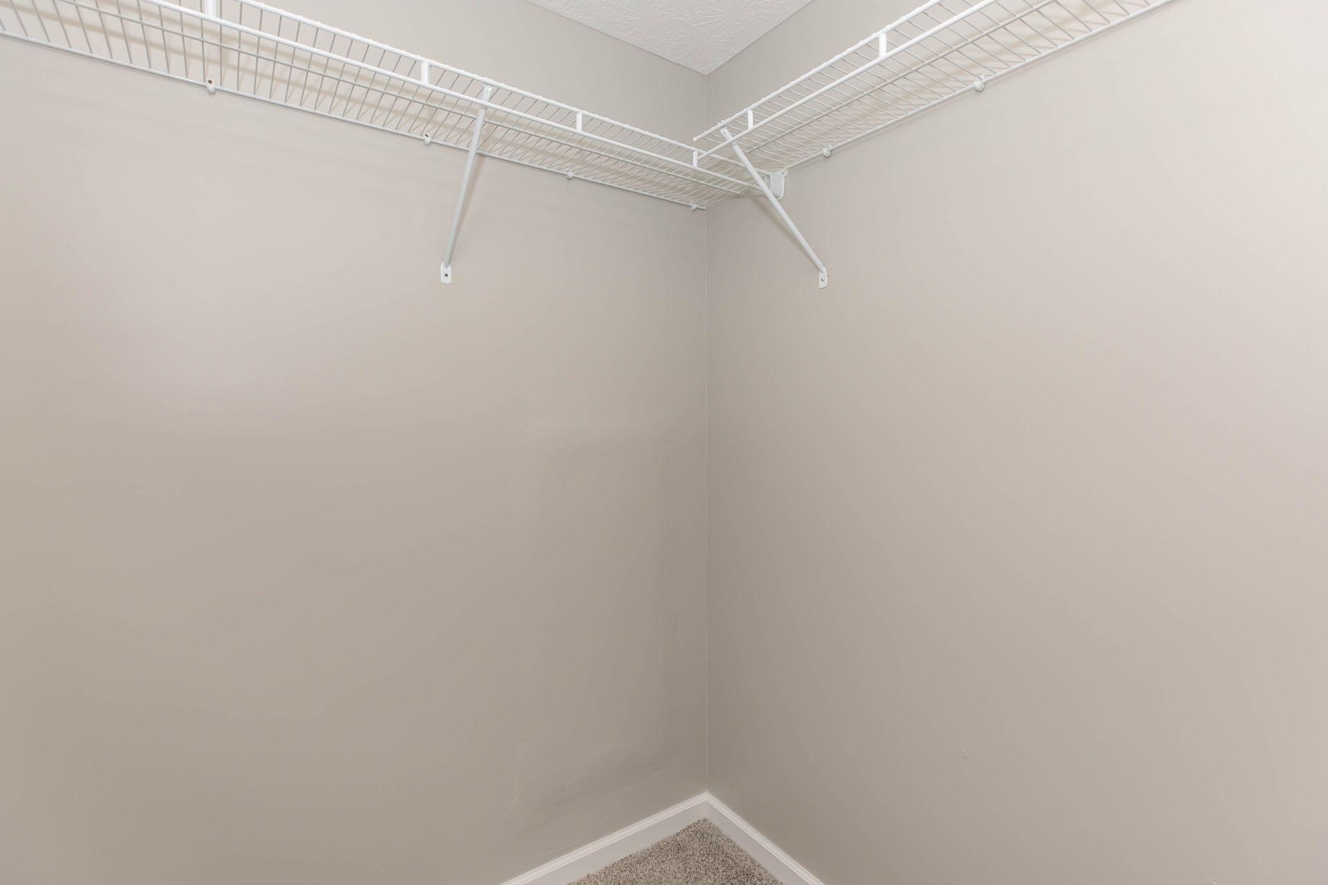 Empty beige closet with wire shelving and carpeted floor corner at Quarry Apartments for Rent in Columbus, OH.