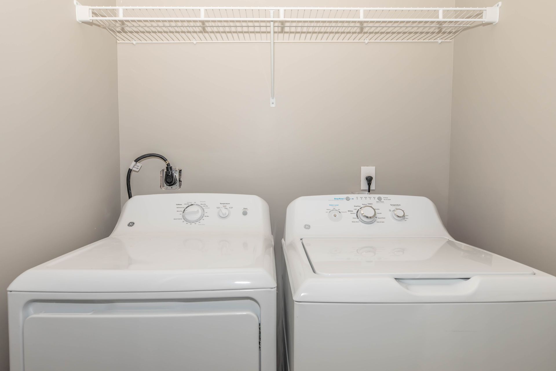 White washer and dryer in a laundry closet with a wire shelf overhead at Quarry Apartments for Rent in Columbus, OH.