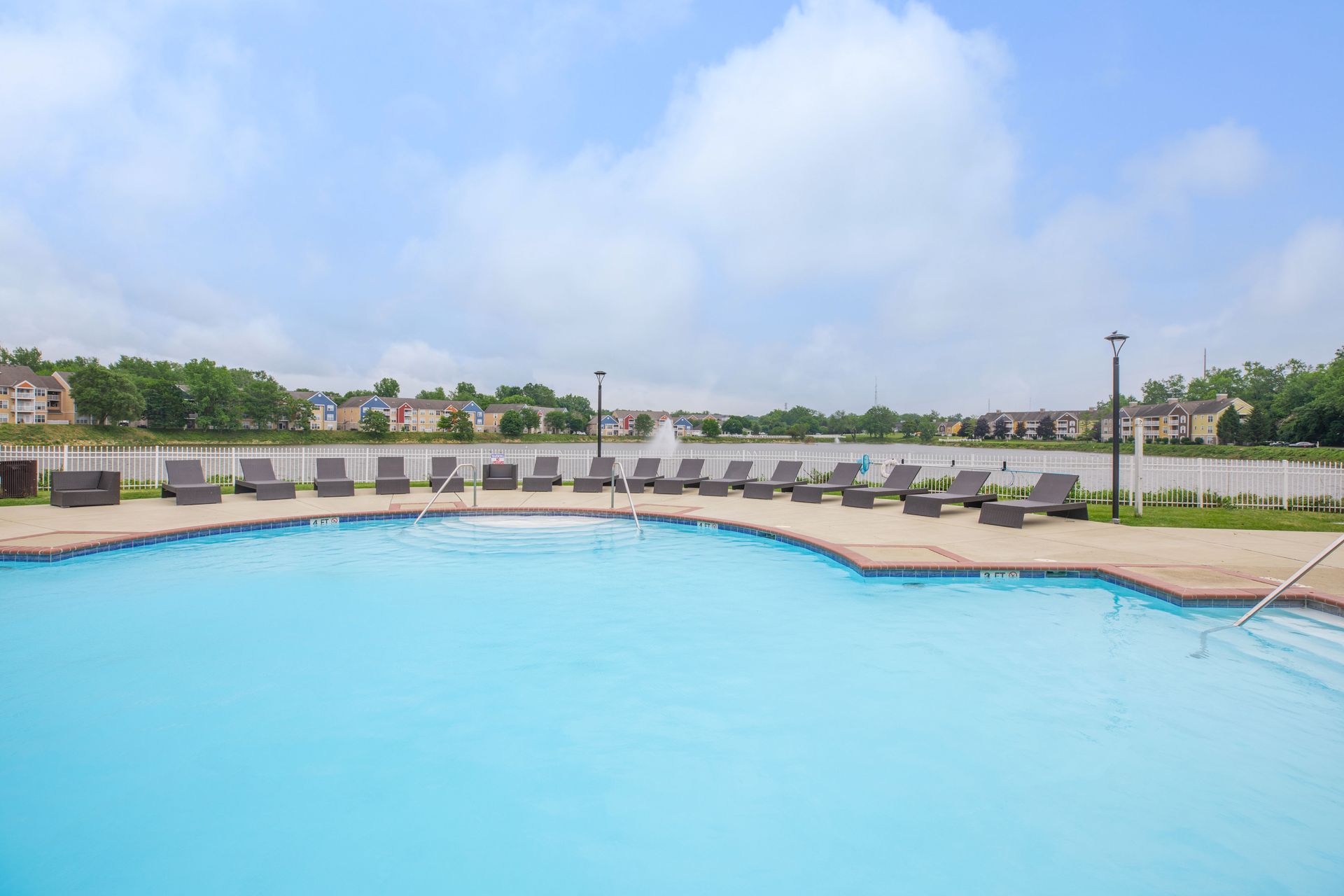 Outdoor swimming pool with clear blue water, lounge chairs, and grassy surroundings under a partly cloudy sky at Quarry Apartments for Rent in Columbus, OH.