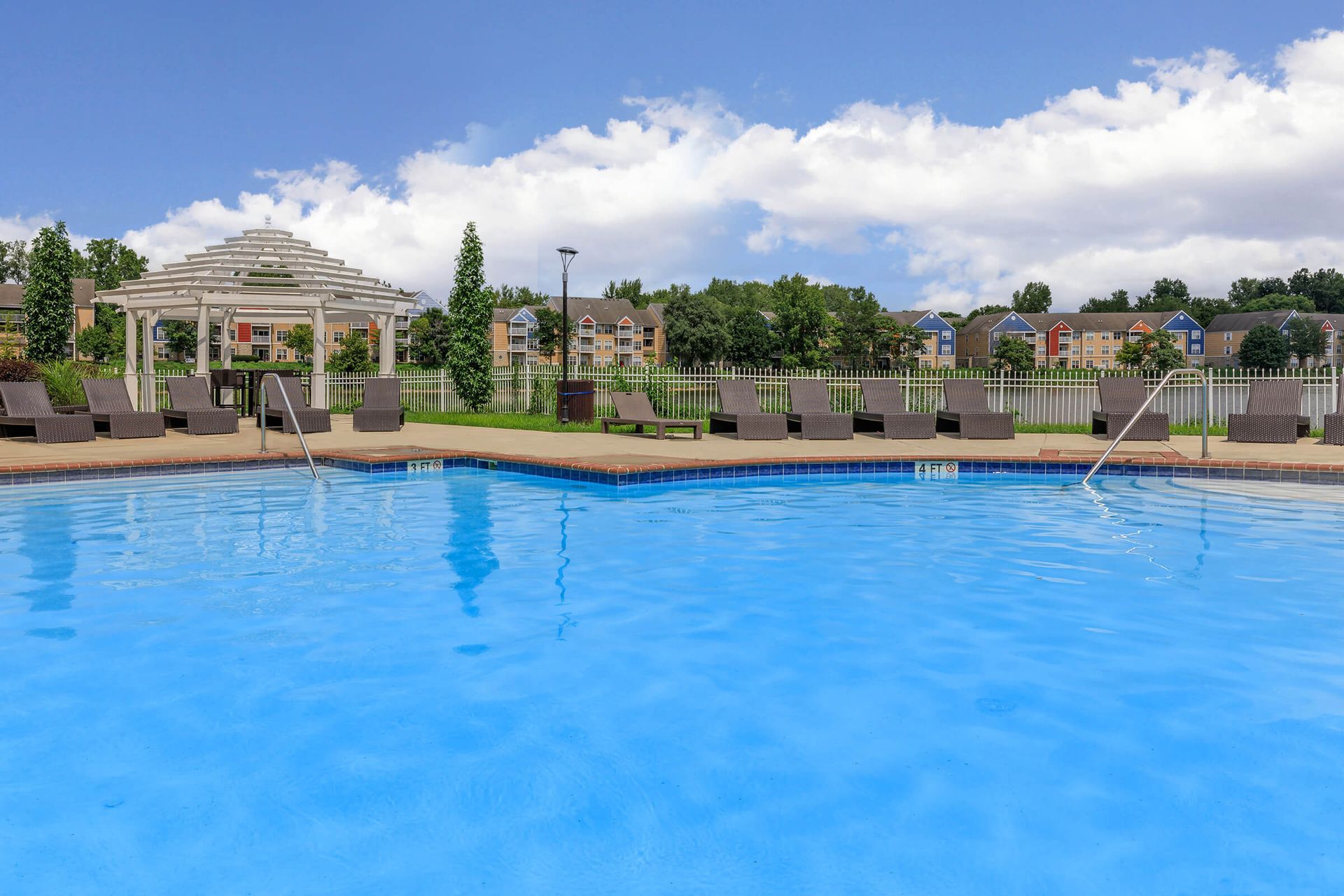 Outdoor swimming pool with blue water, lounge chairs, and palm trees under a cloudy sky at Quarry Apartments for Rent in Columbus, OH.