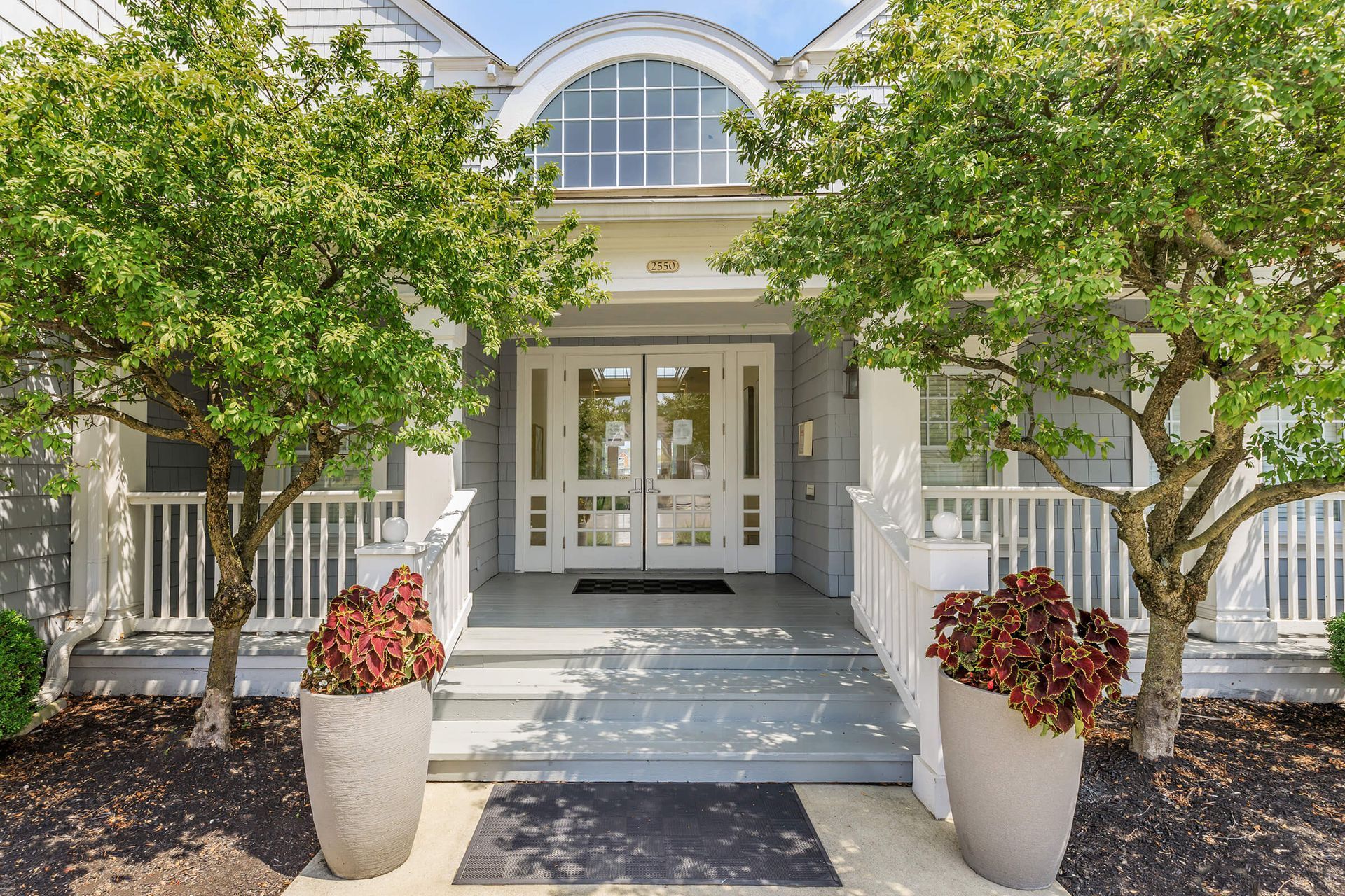 Front entrance of a white house with columns, arched window, and potted flowers on the walkway at Quarry Apartments for Rent in Columbus, OH.