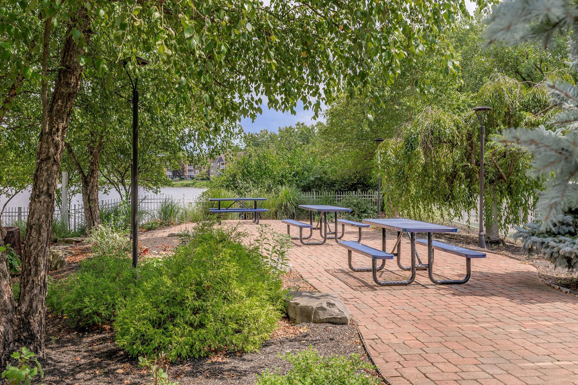 Brick-paved park patio with picnic tables under leafy trees and greenery at Quarry Apartments for Rent in Columbus, OH.