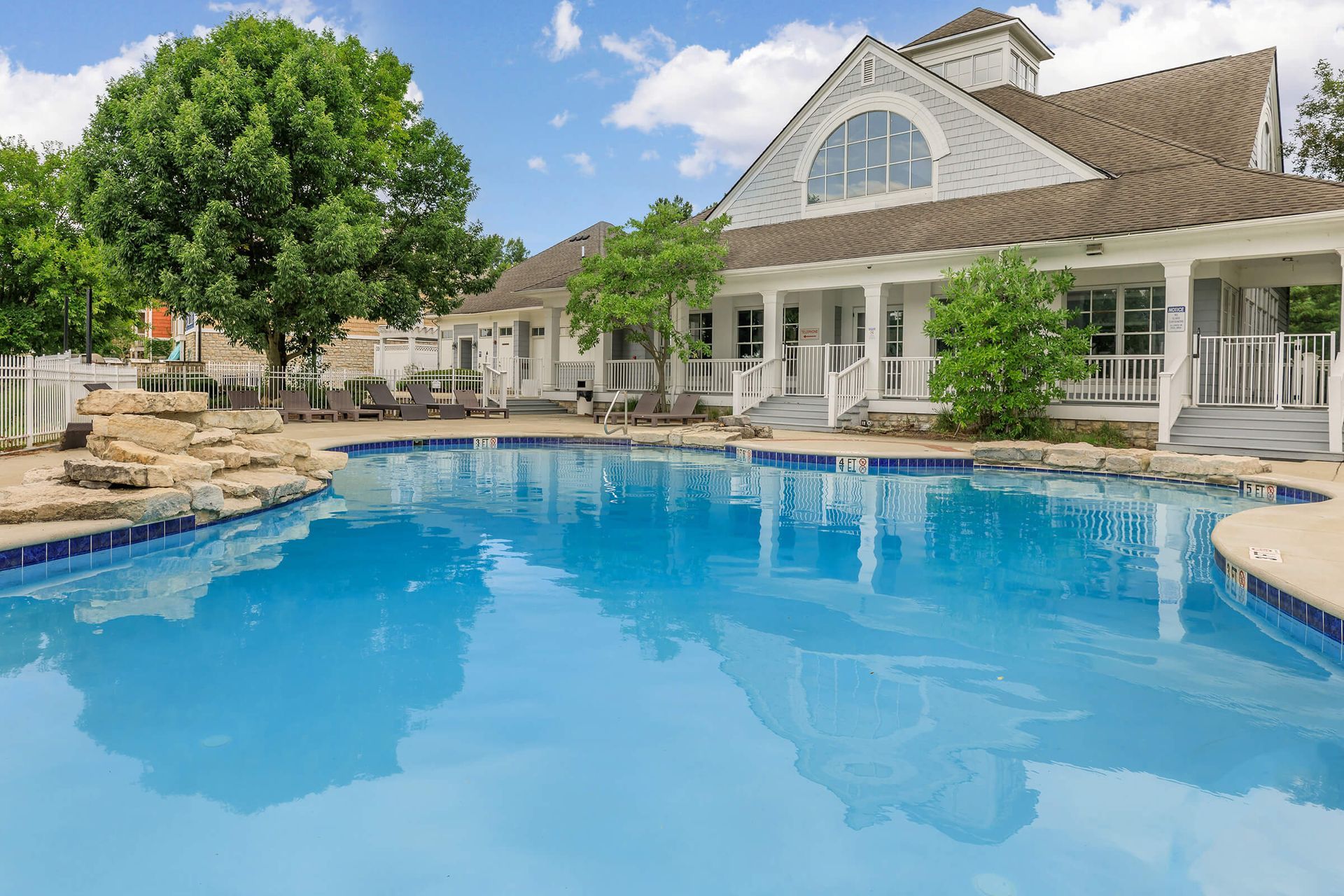 Luxury backyard pool with blue water, patio lounge chairs, and a white house with a large arched window at Quarry Apartments for Rent in Columbus, OH.
