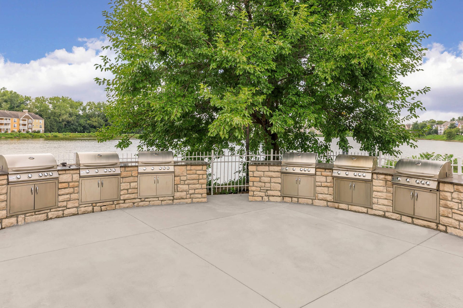 Patio overlooking a river, stone wall, and large green tree under a partly cloudy sky at Quarry Apartments for Rent in Columbus, OH.