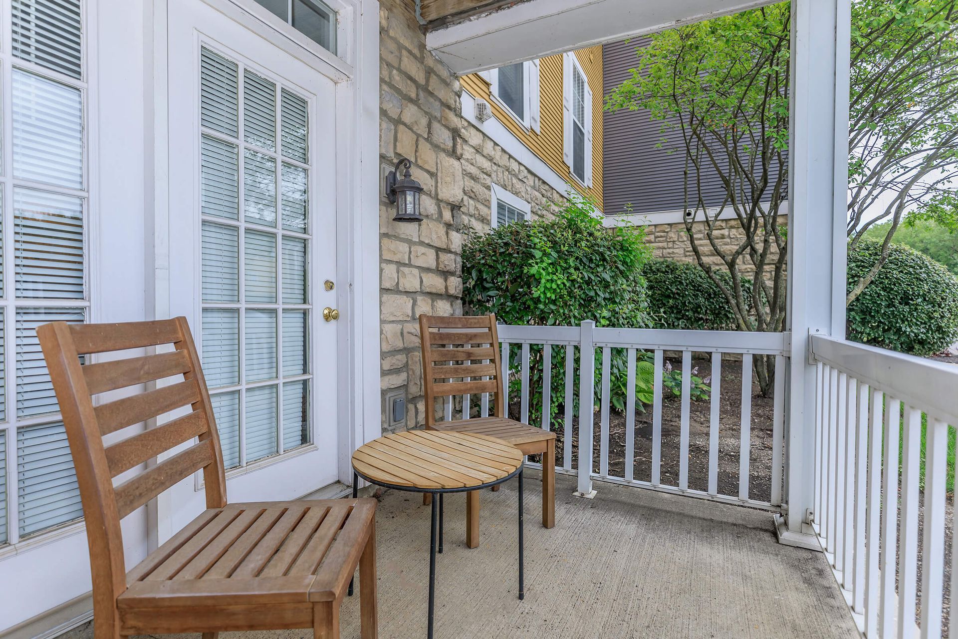 Wooden chairs and table on a porch, near a door. Brick wall and white railing visible at Quarry Apartments for Rent in Columbus, OH.