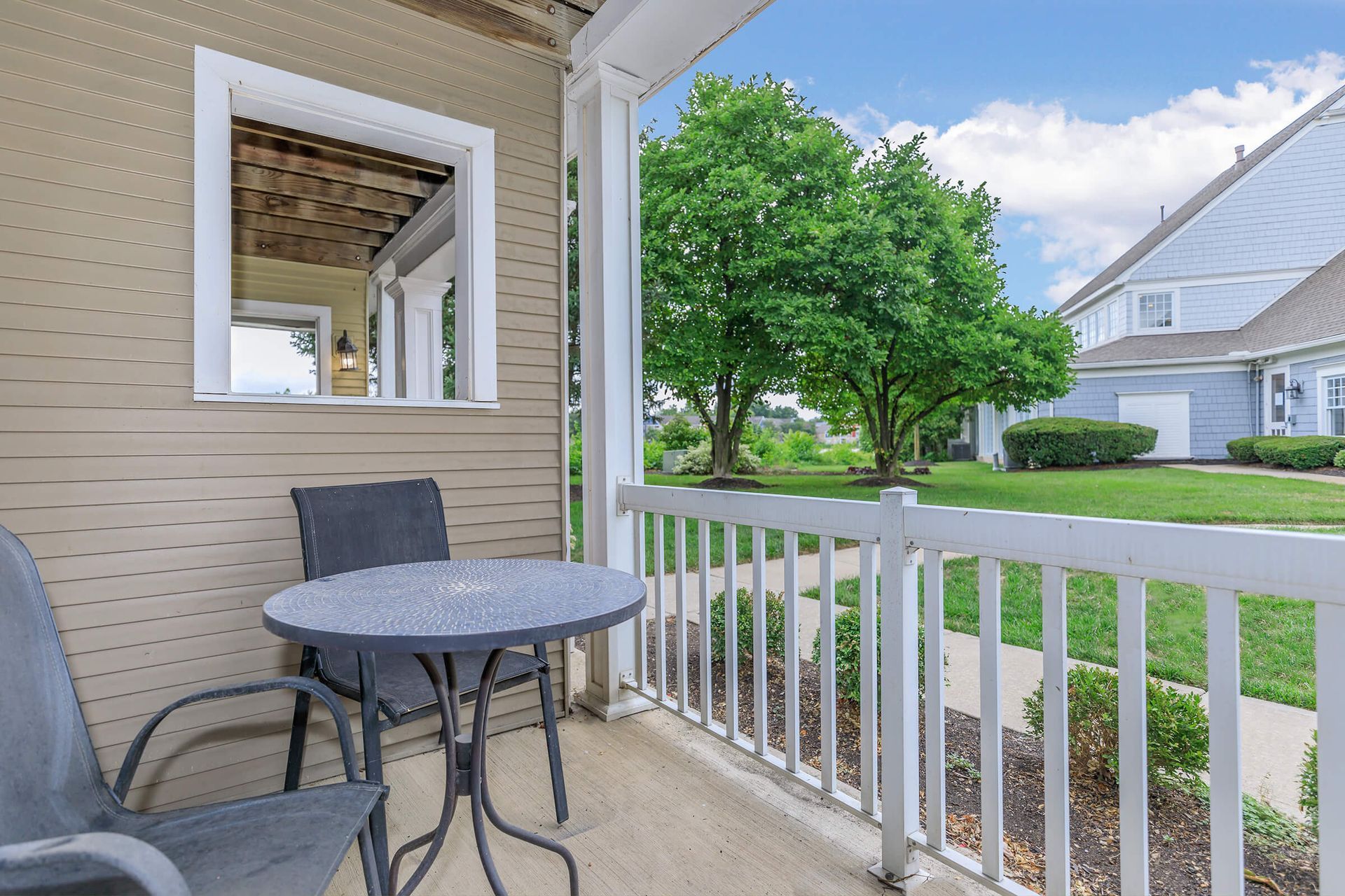 Covered front porch with gray table, chairs, and a view of a green lawn and white house at Quarry Apartments for Rent in Columbus, OH.