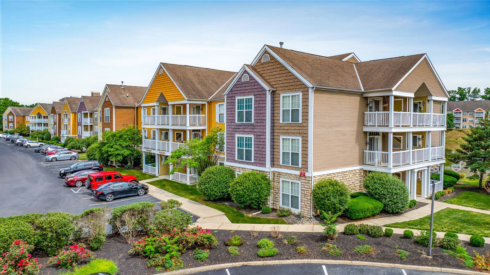 Apartment complex with tan and brick buildings, balconies, parked cars, and landscaped grounds at Quarry Apartments for Rent in Columbus, OH.