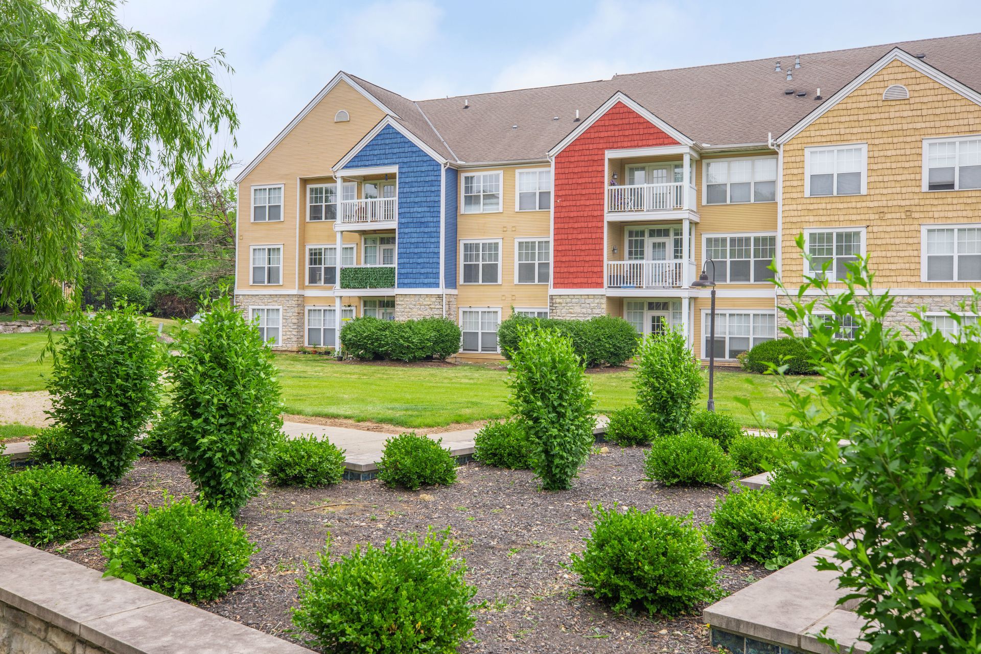 Colorful apartment building with landscaped shrubs and green trees in front at Quarry Apartments for Rent in Columbus, OH.