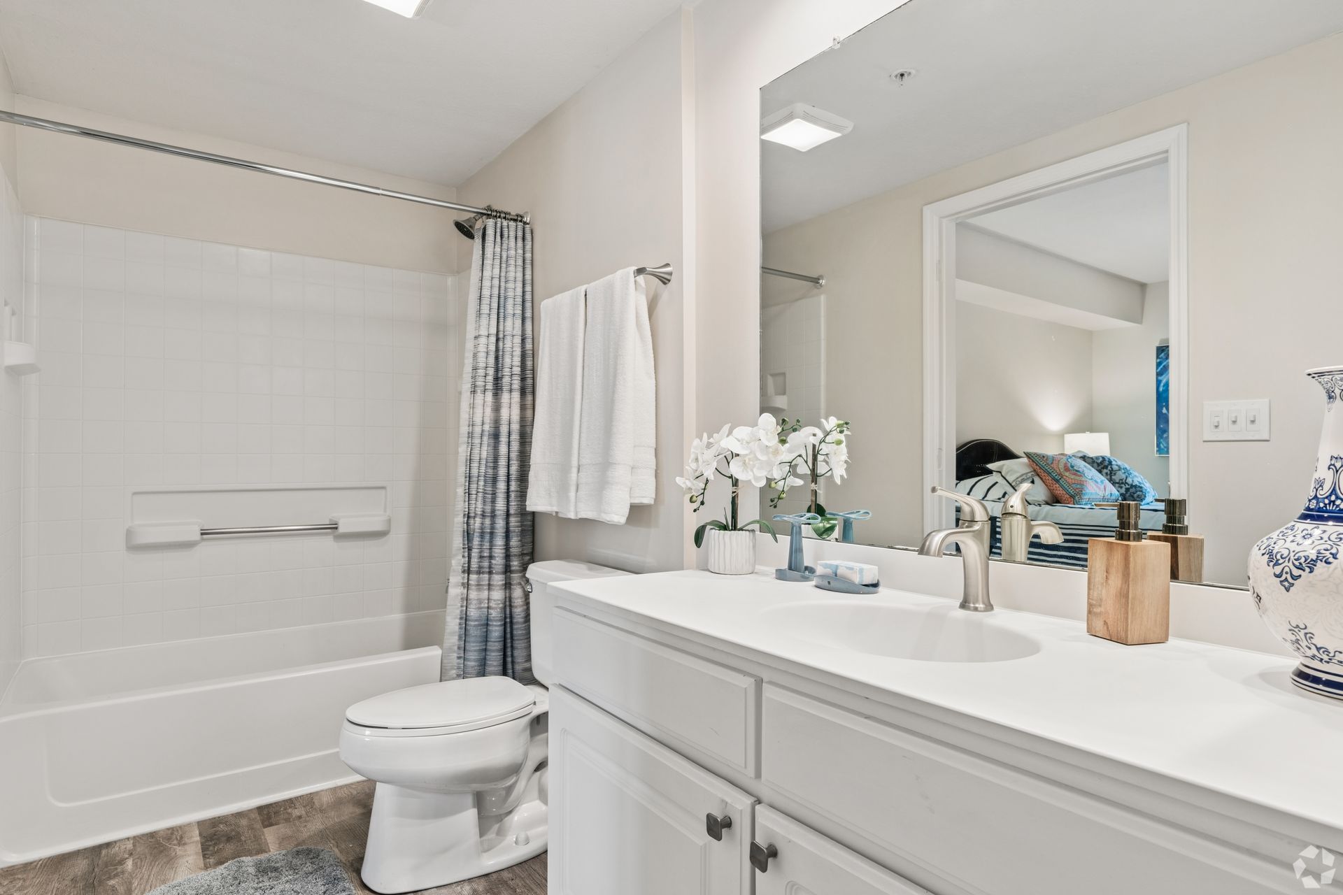 Bright bathroom with tub-shower, toilet, and white vanity with flowers and mirror at Quarry Apartments for Rent in Columbus, OH.