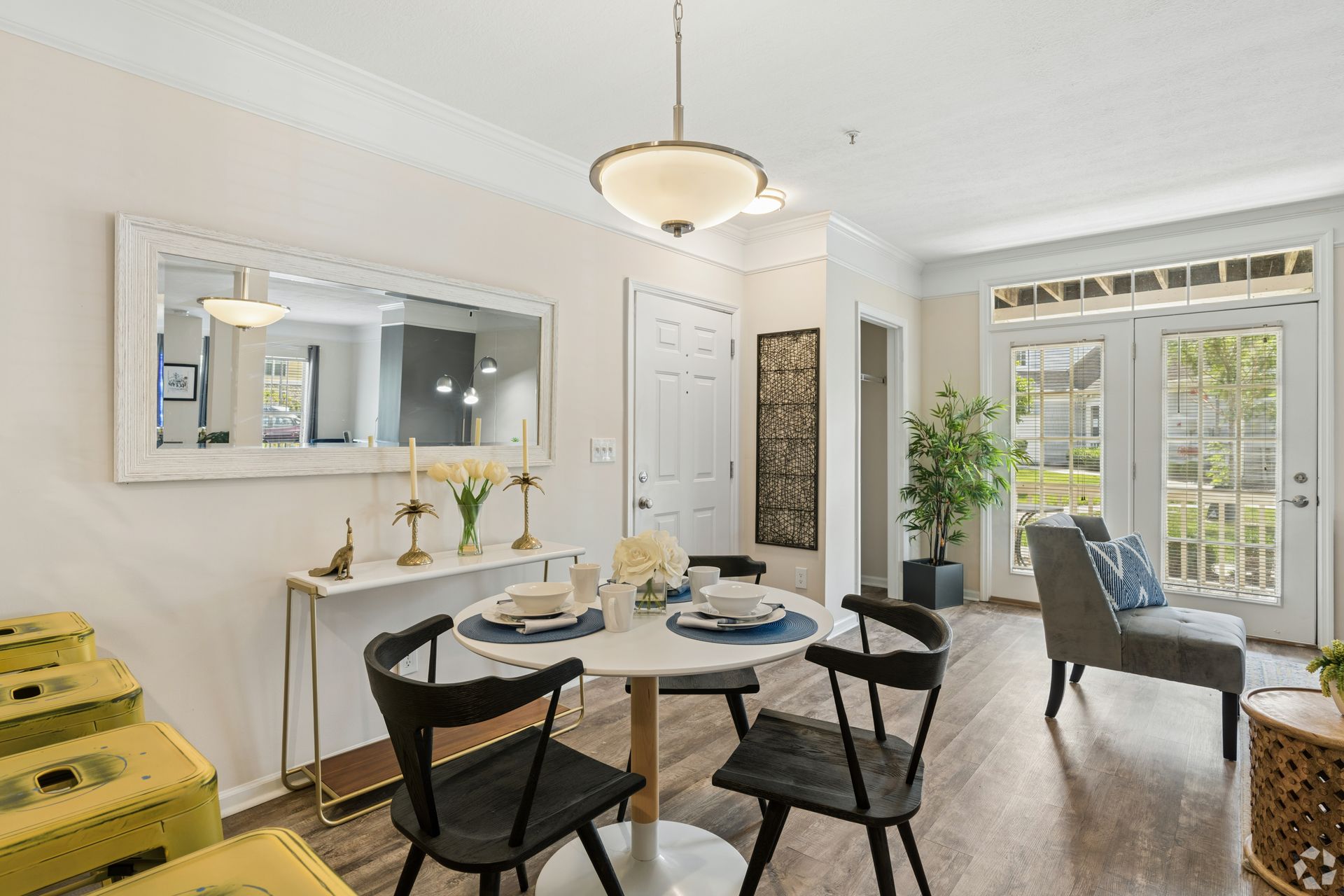Bright dining room with round table, black chairs, mirror, and French doors to a patio at Quarry Apartments for Rent in Columbus, OH.