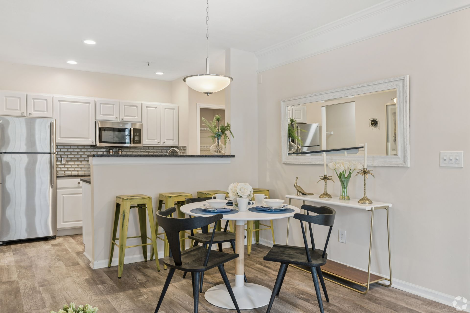 Bright kitchen and dining area with white cabinets, stainless appliances, and a black round table with chairs at Quarry Apartments for Rent in Columbus, OH.