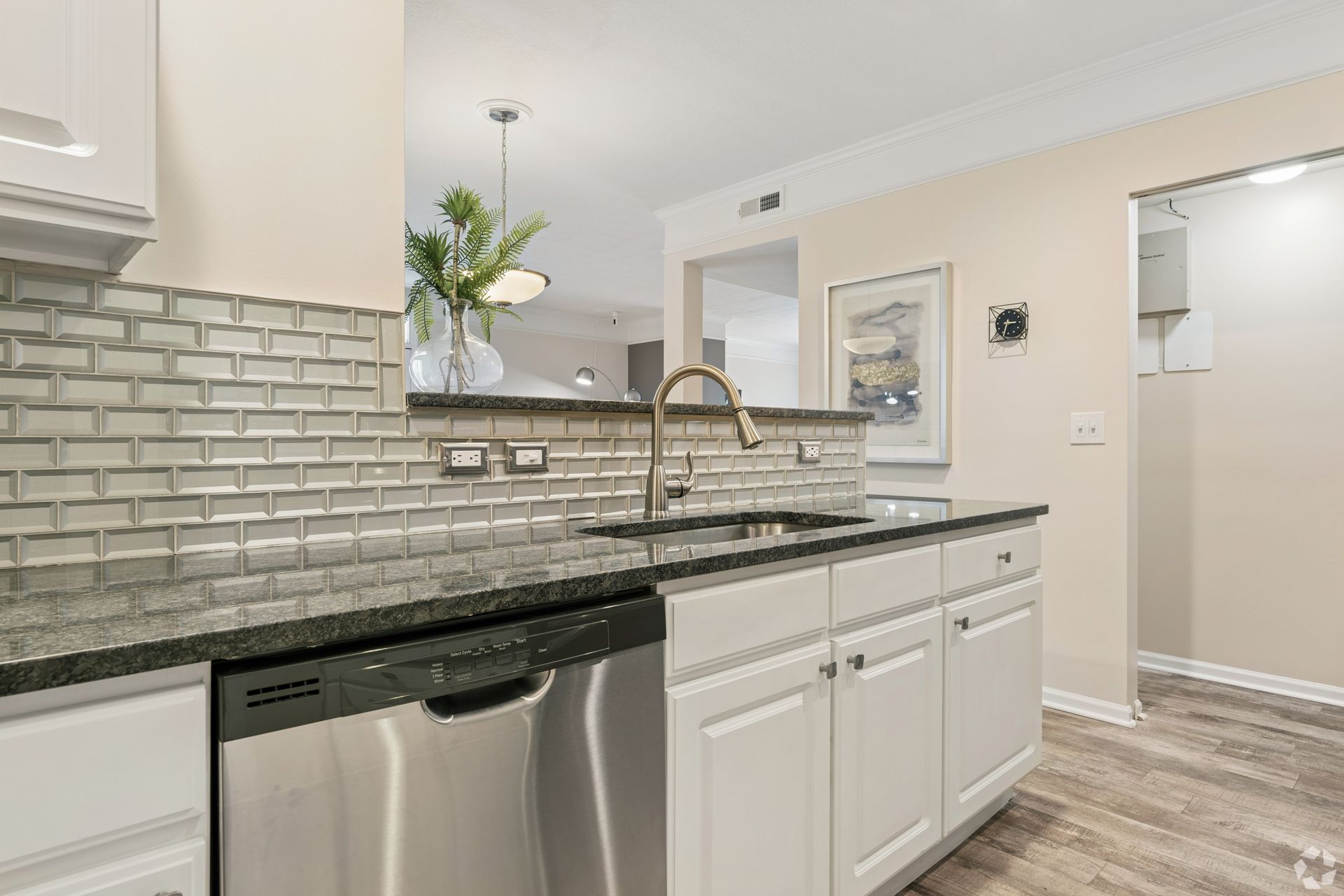 Bright kitchen with white cabinets, gray tile backsplash, granite counter, and stainless dishwasher at Quarry Apartments for Rent in Columbus, OH