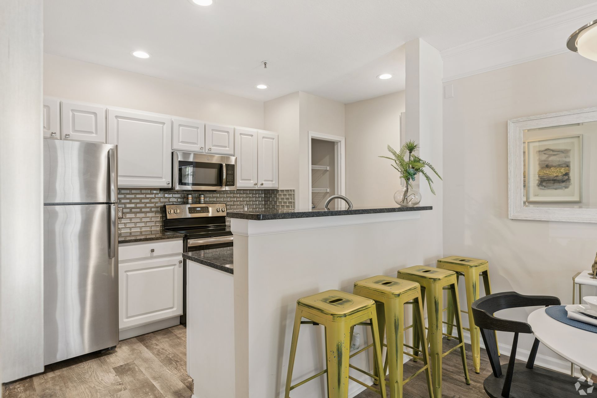 Bright kitchen with white cabinets, stainless steel appliances, and yellow bar stools at a counter at Quarry Apartments for Rent in Columbus, OH