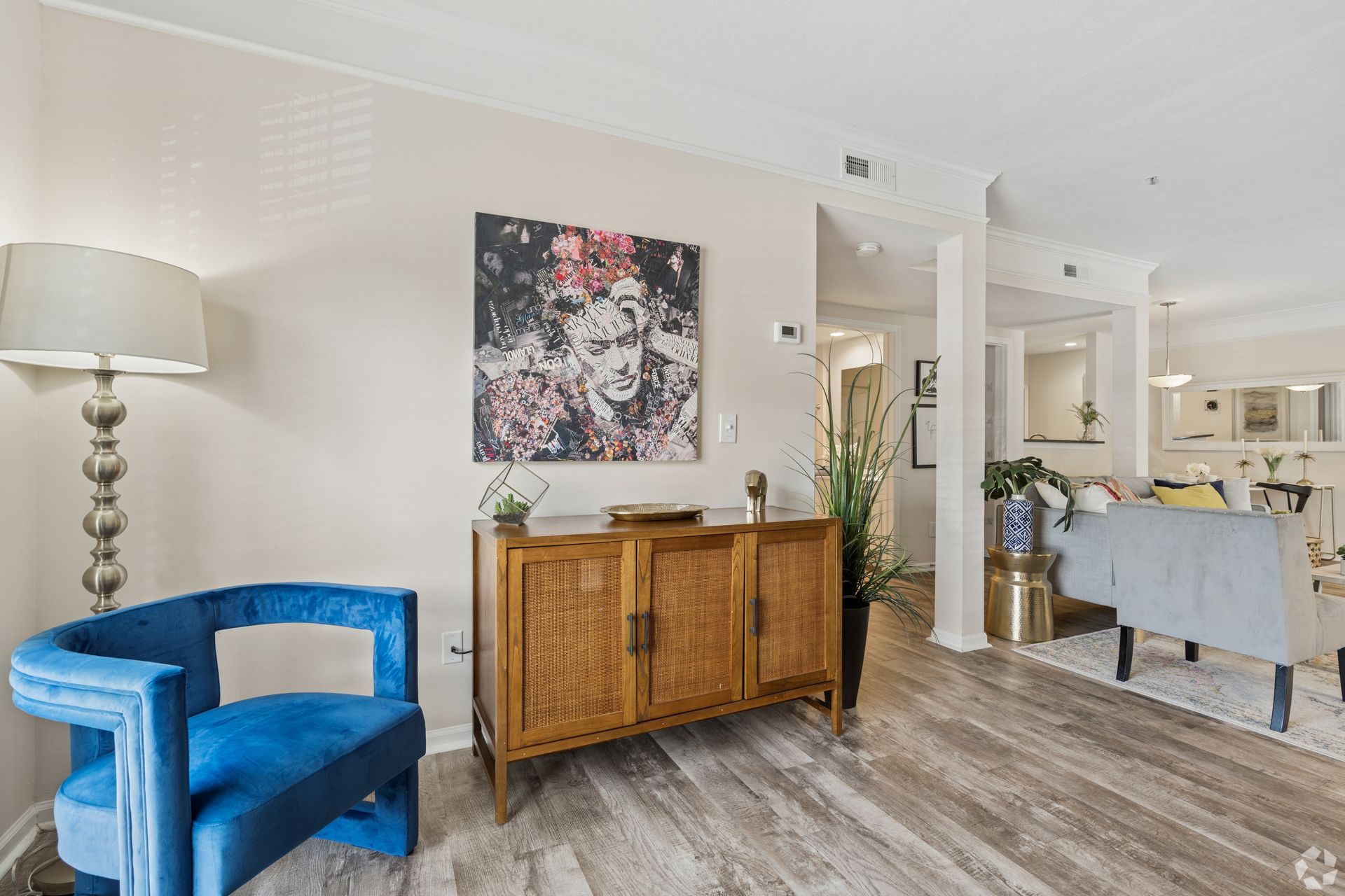 Bright living room with blue chair, wood sideboard, floral wall art, and dining area beyond at Quarry Apartments for Rent in Columbus, OH.