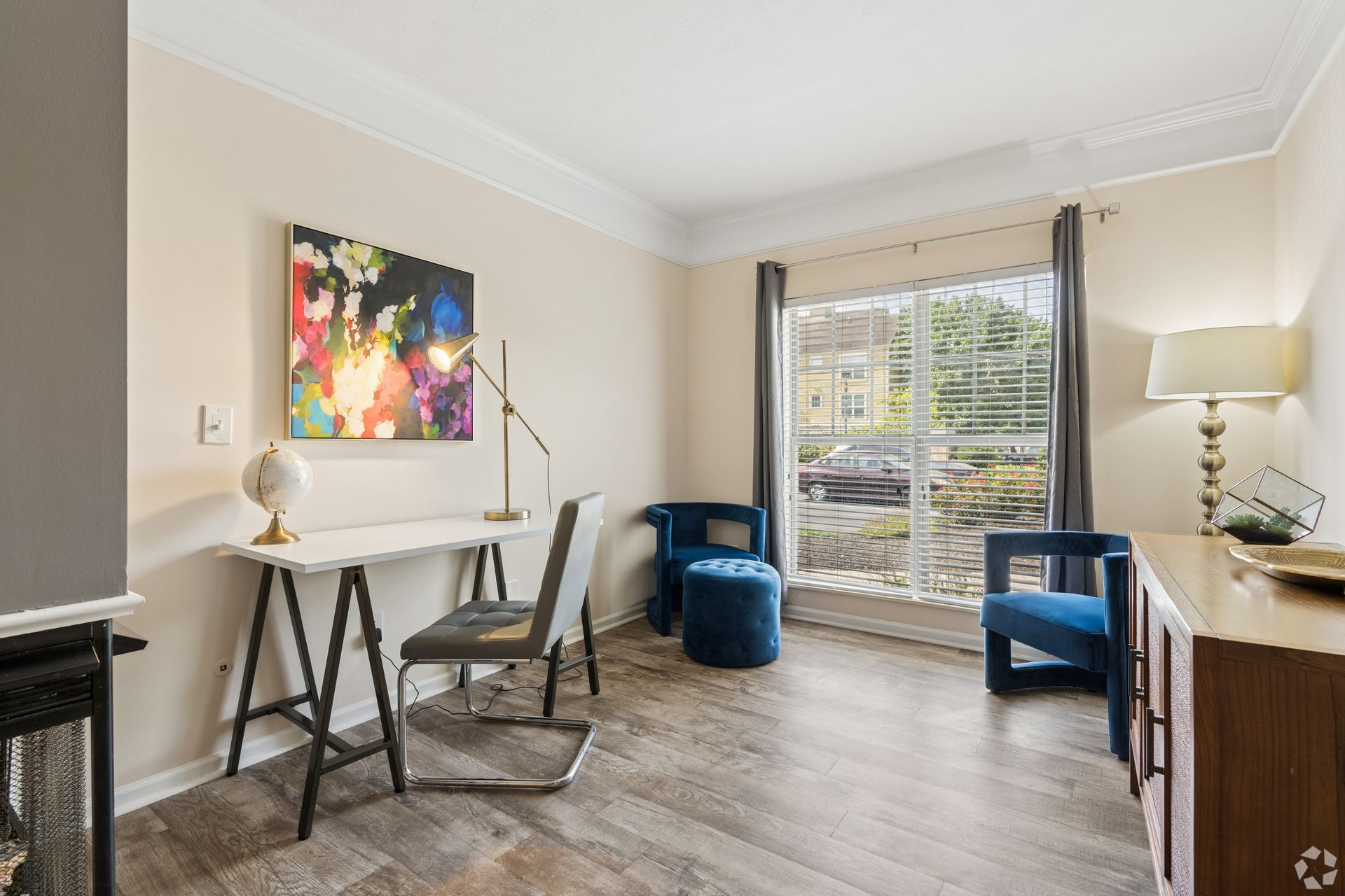 Bright home office with desk, chair, blue armchair, floor lamp, and large window overlooking apartments at Quarry Apartments for Rent in Columbus, OH.