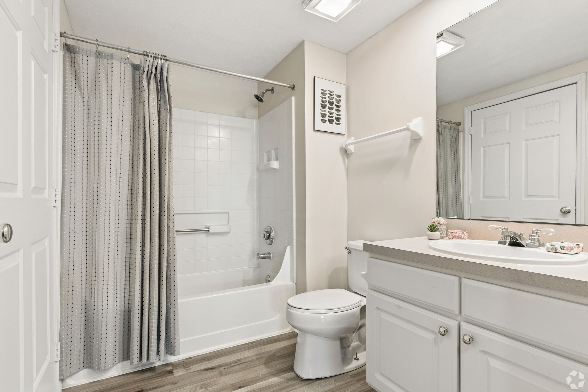 Bright white bathroom with tub-shower, toilet, vanity, and mirror under soft lighting at Quarry Apartments for Rent in Columbus, OH.