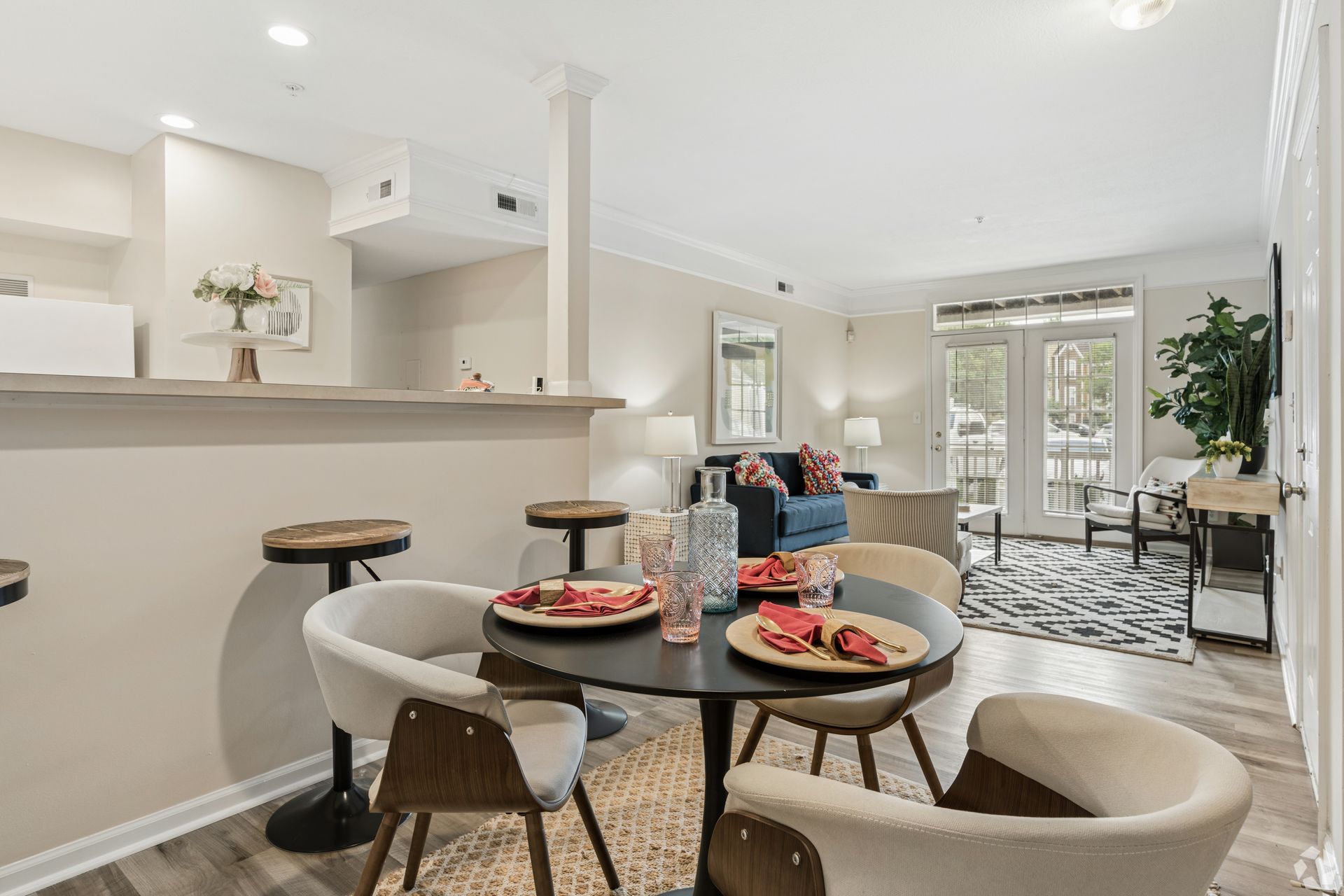 Bright open dining and living room with a round table set for dessert and a view of a patio at Quarry Apartments for Rent in Columbus, OH.
