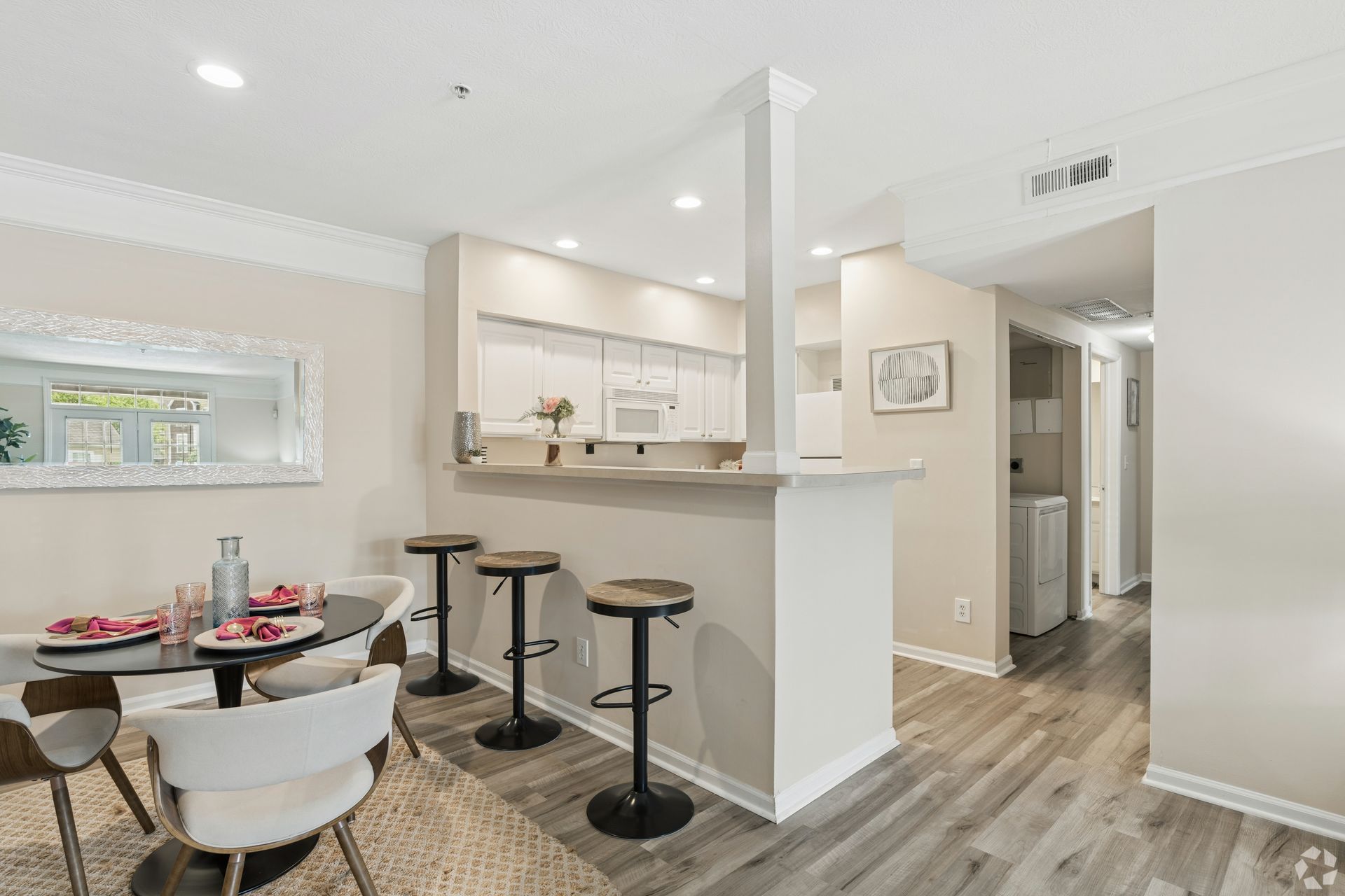 Bright open kitchen and dining area with bar stools, white cabinets, and wood-look flooring at Quarry Apartments for Rent in Columbus, OH.