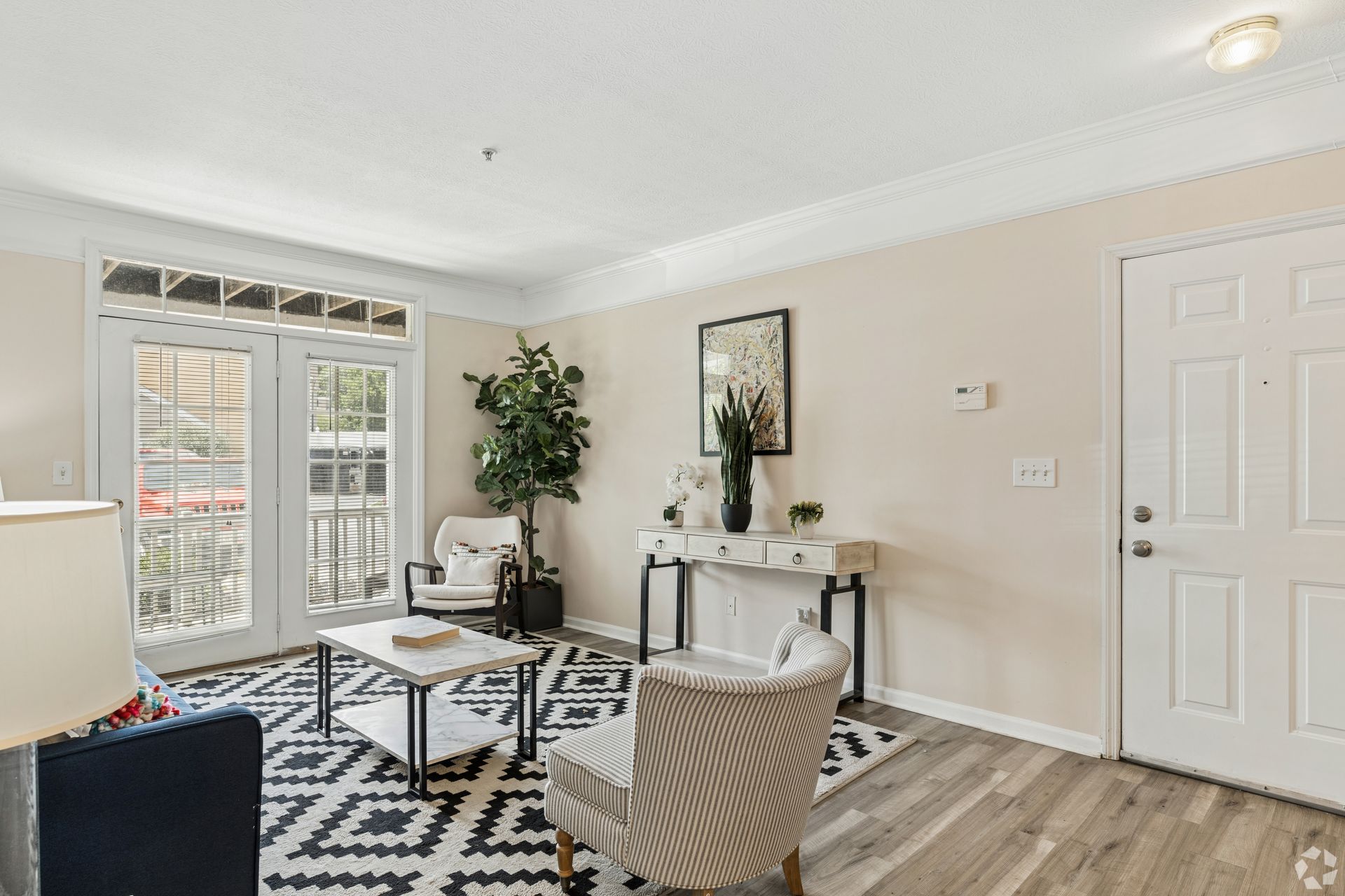 Bright living room with patterned rug, beige chairs, console table, plant, and front door at Quarry Apartments for Rent in Columbus, OH.