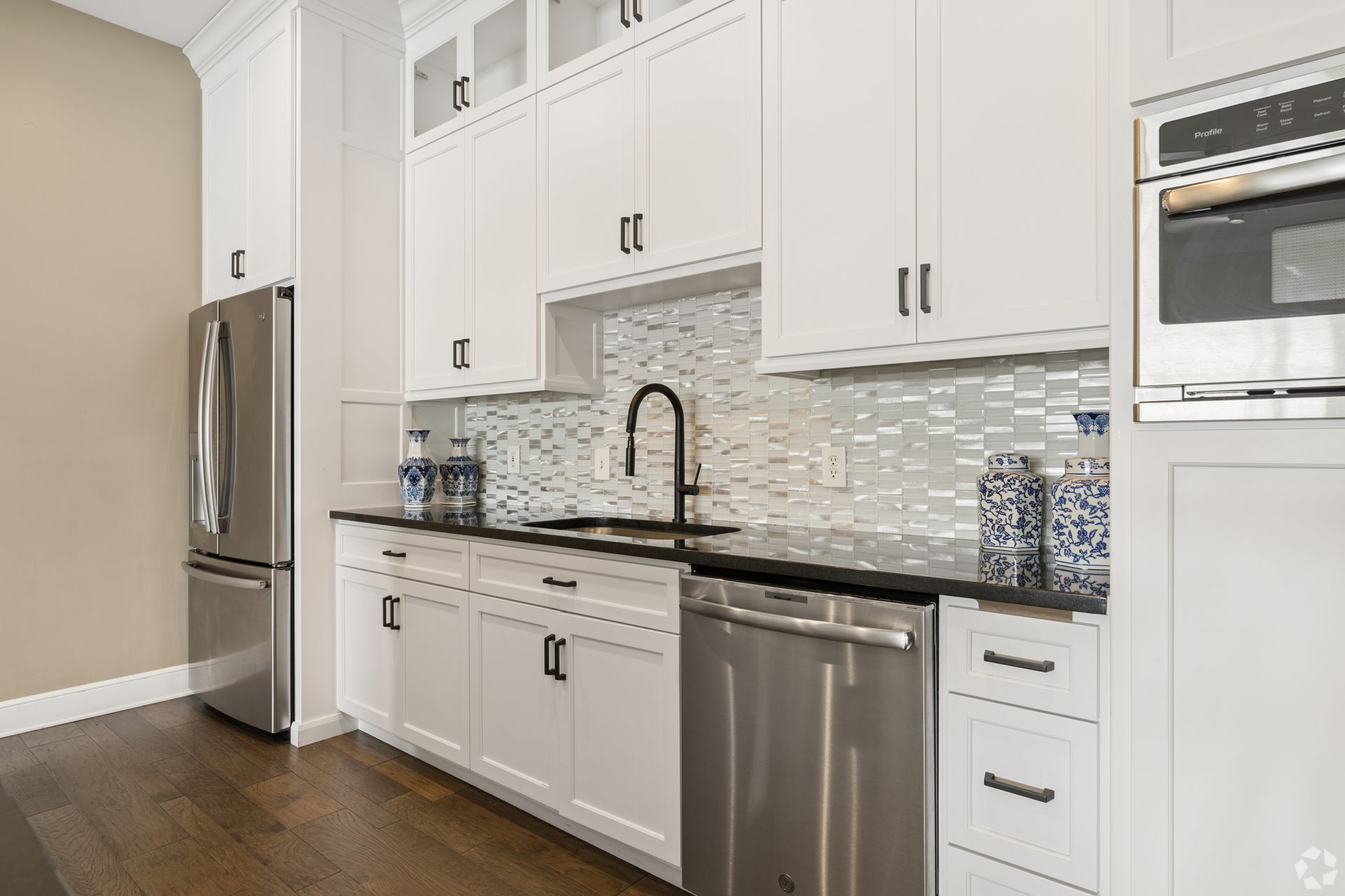 Modern white kitchen with stainless steel appliances, mosaic backsplash, and dark wood floors at Quarry Apartments for Rent in Columbus, OH.