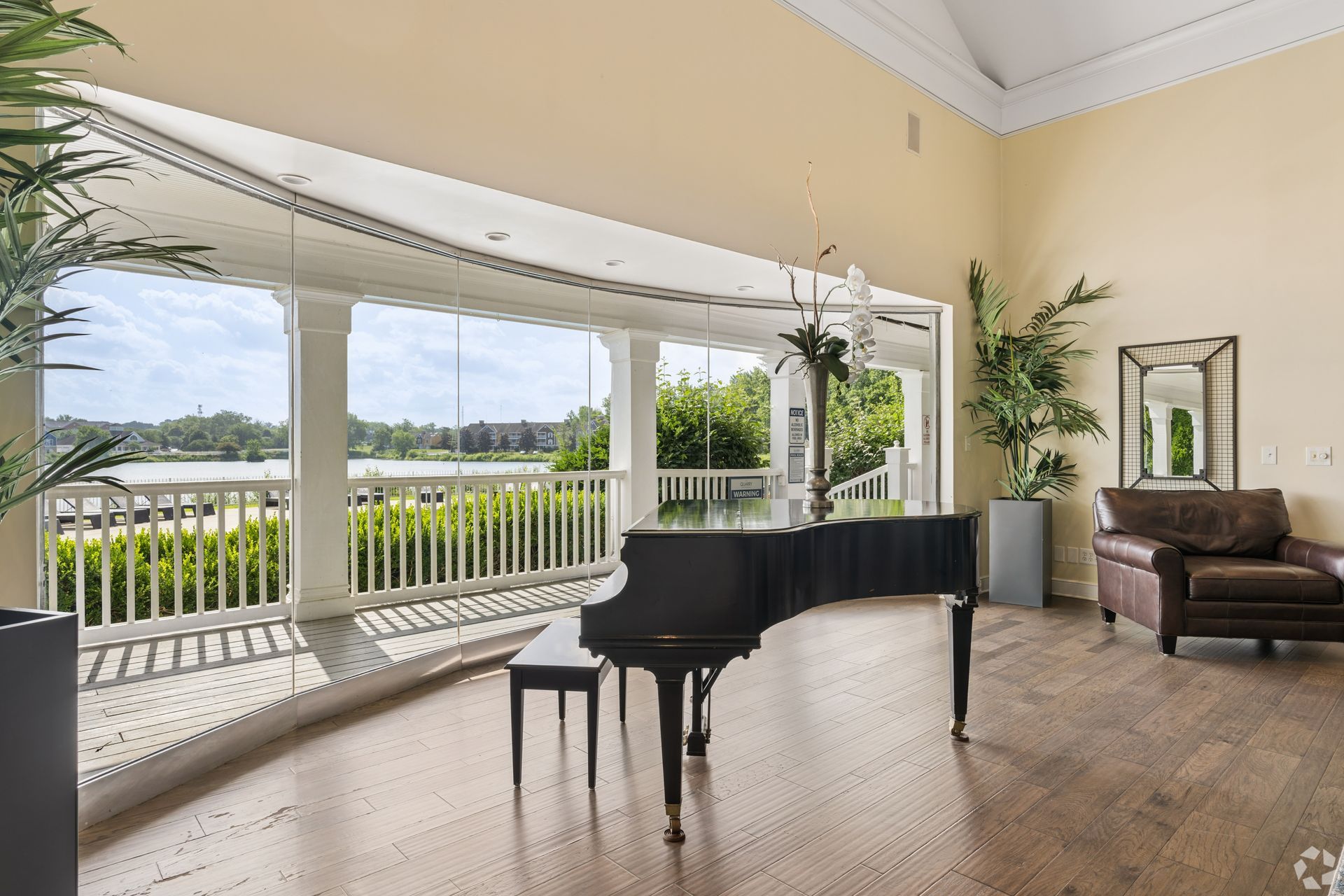 Bright living room with a black grand piano, large windows, and a lake view at Quarry Apartments for Rent in Columbus, OH.