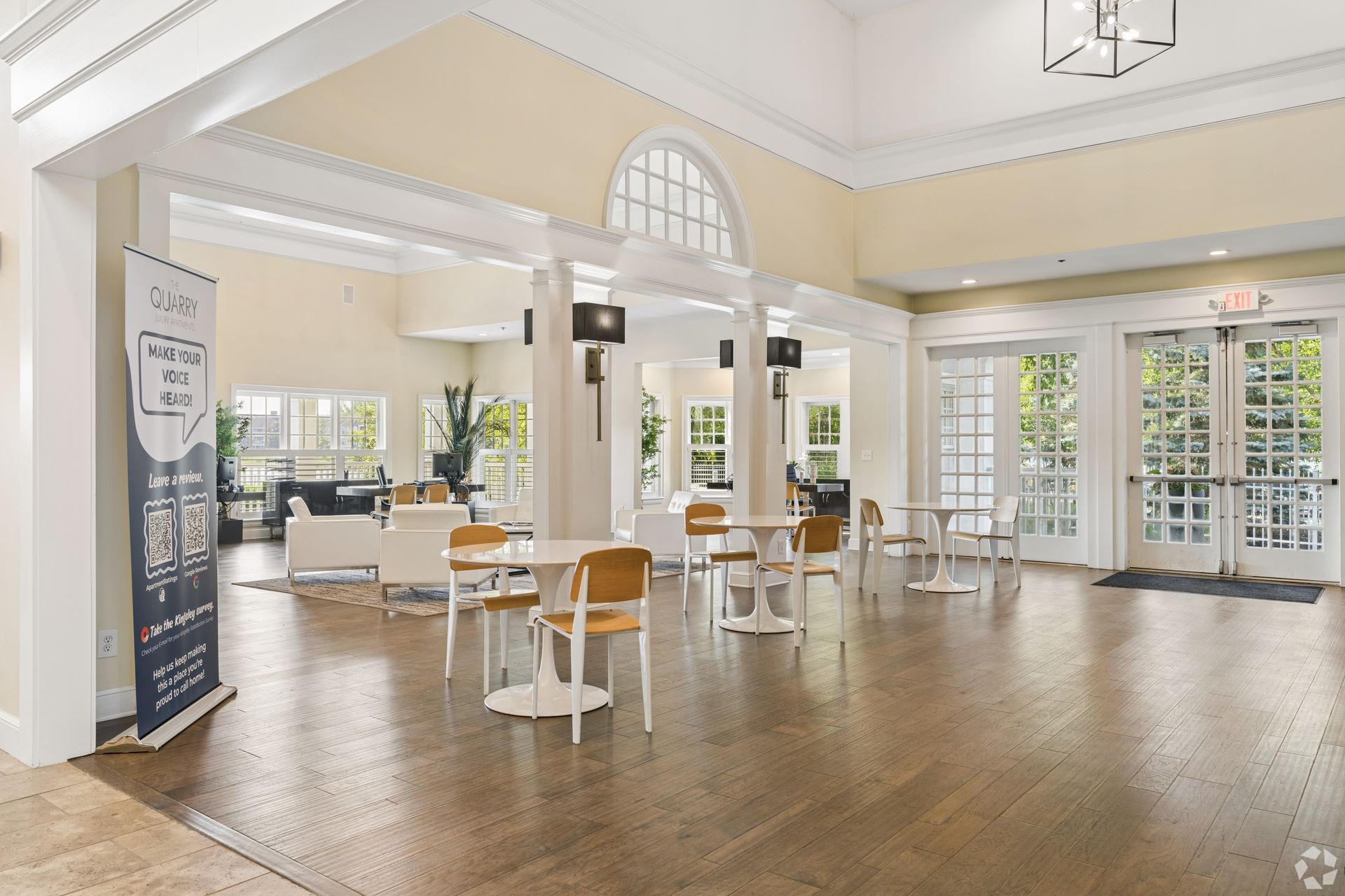 Bright, airy lobby with white columns, arched windows, tables, and chairs on a polished wood floor at Quarry Apartments for Rent in Columbus, OH.