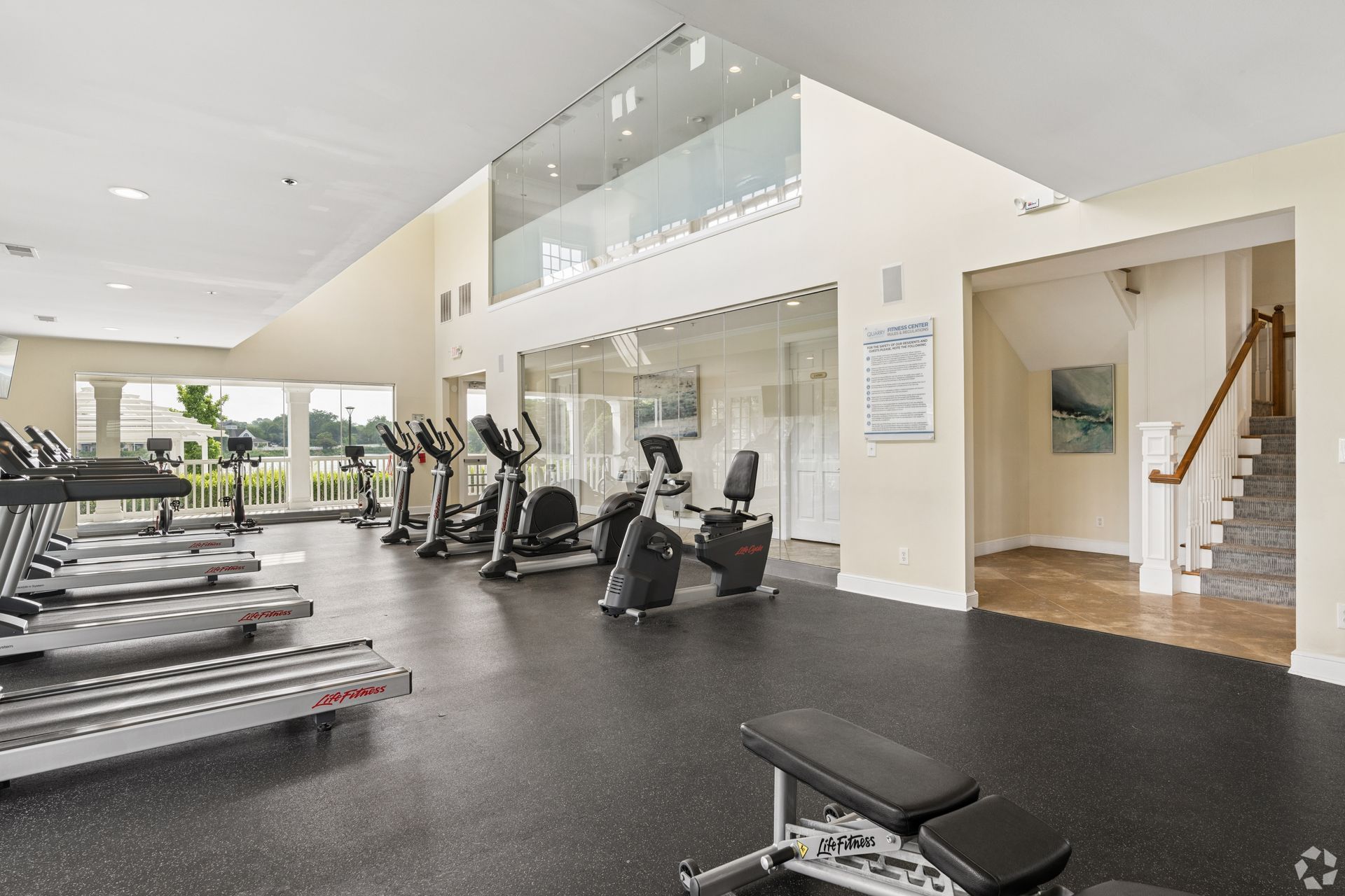 Bright gym with treadmills, stationary bikes, and a stairway by a lounge area at Quarry Apartments for Rent in Columbus, OH.