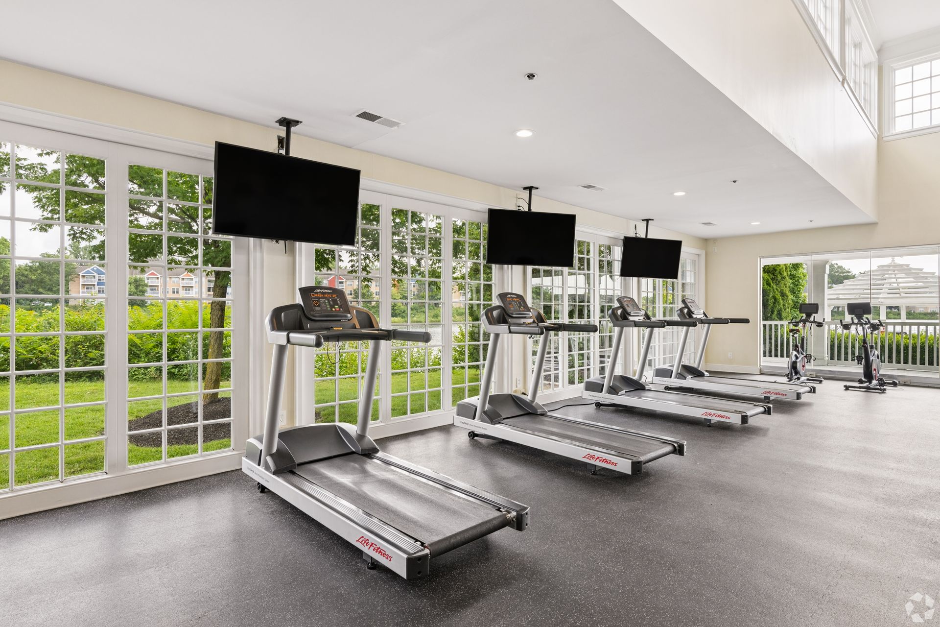 Bright gym with row of treadmills, wall mirrors, and large windows overlooking greenery at Quarry Apartments for Rent in Columbus, OH.