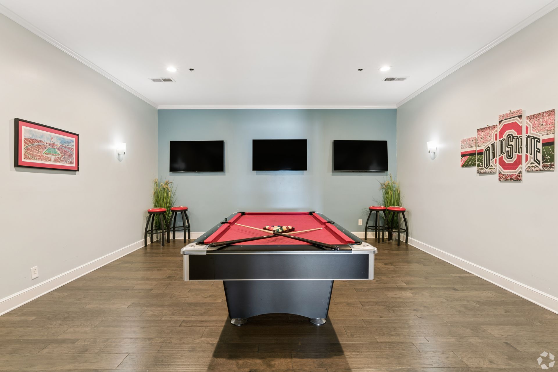 Modern game room with pool table, wall-mounted TVs, gray walls, and hardwood floors at Quarry Apartments for Rent in Columbus, OH.