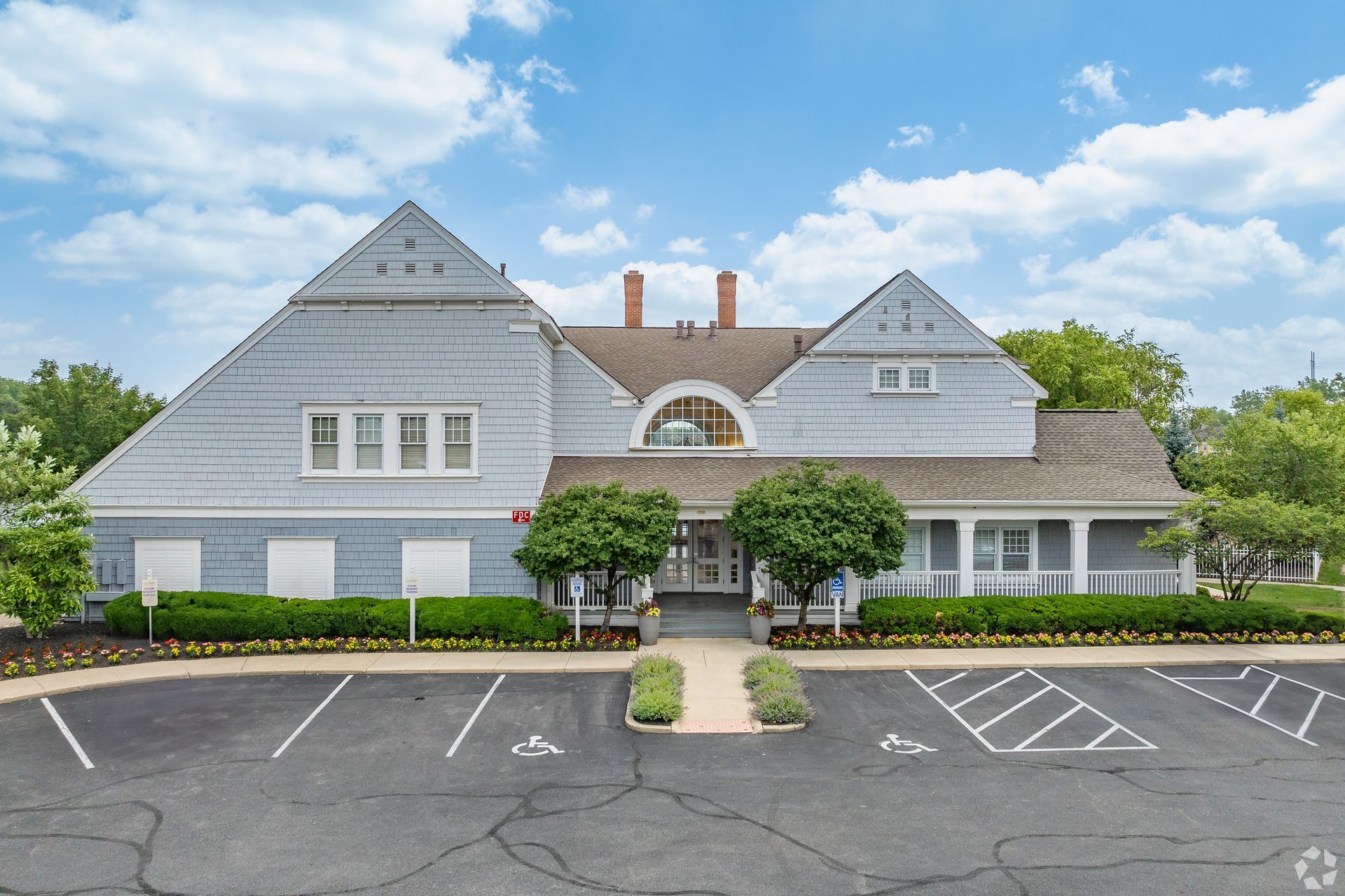 Large gray shingled building with white trim, arched entrance, and empty parking lot under a blue sky at Quarry Apartments for Rent in Columbus, OH.