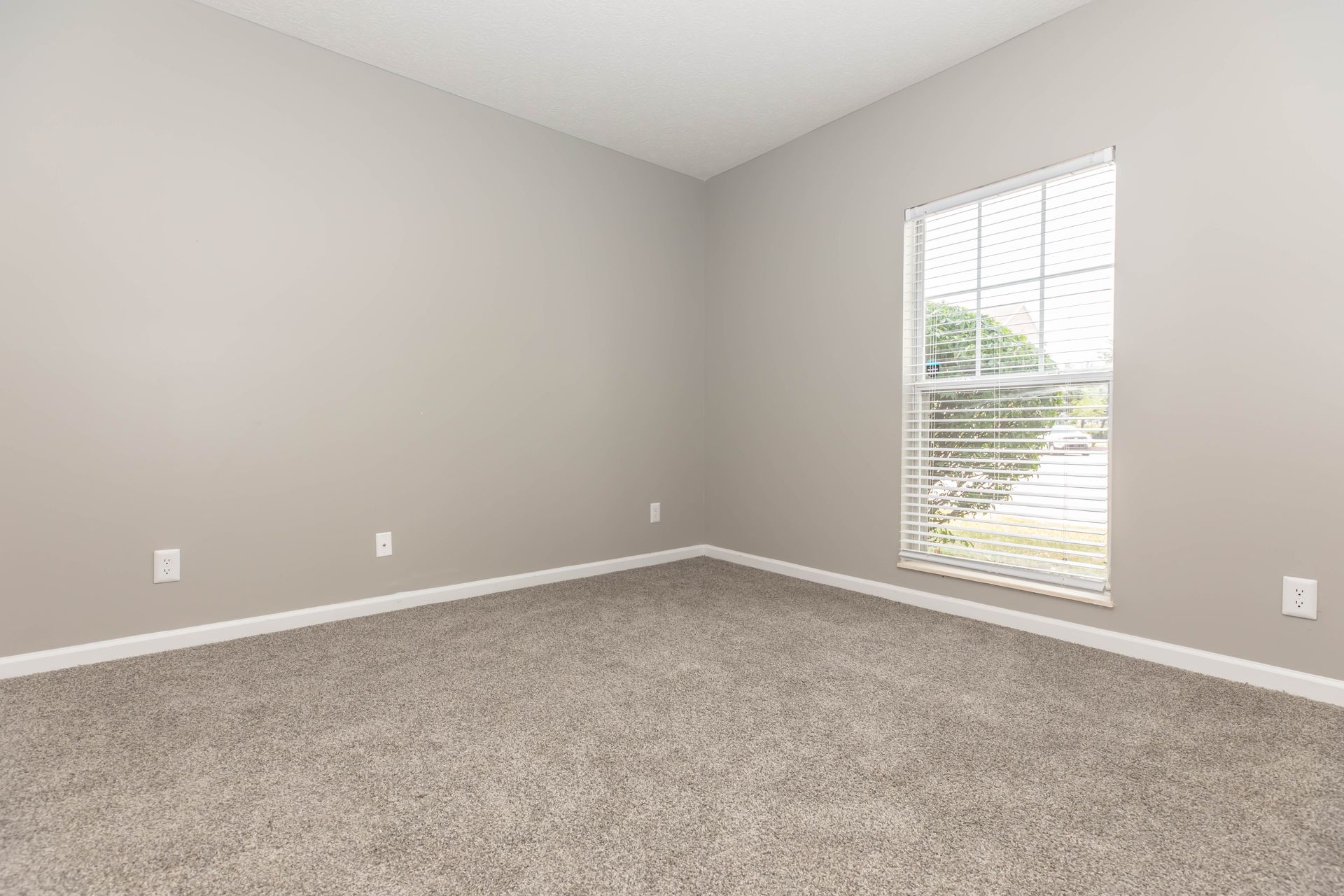 Empty beige bedroom with carpet and a window with white blinds at Quarry Apartments for Rent in Columbus, OH.