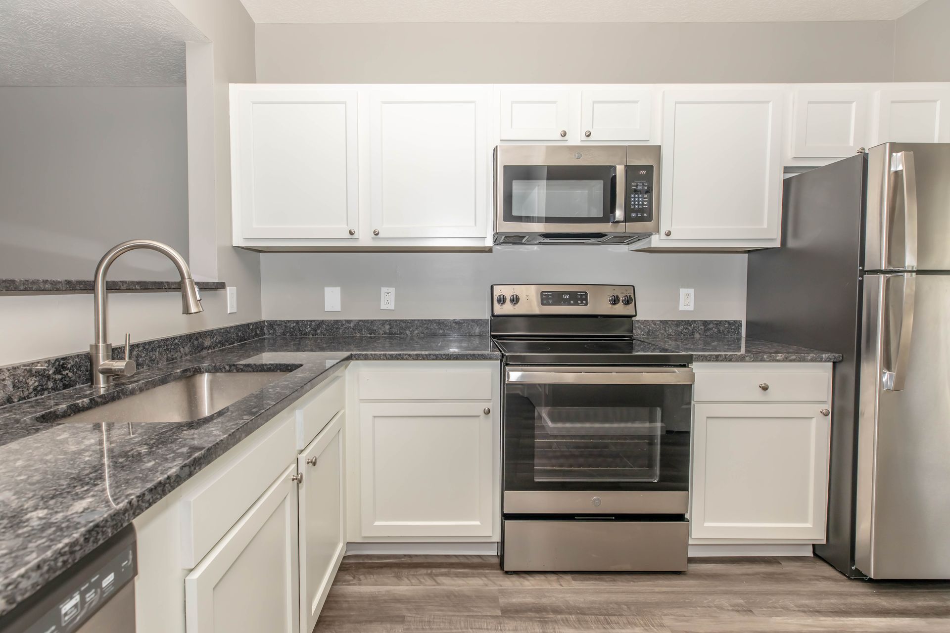 Modern kitchen with stainless steel appliances, white cabinets, and gray granite countertops at Quarry Apartments for Rent in Columbus, OH.