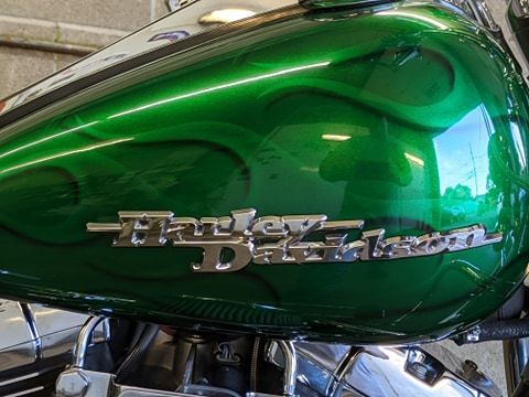 A glossy emerald green Harley-Davidson motorcycle fuel tank with a silver emblem and subtle ghost flame paint accents.