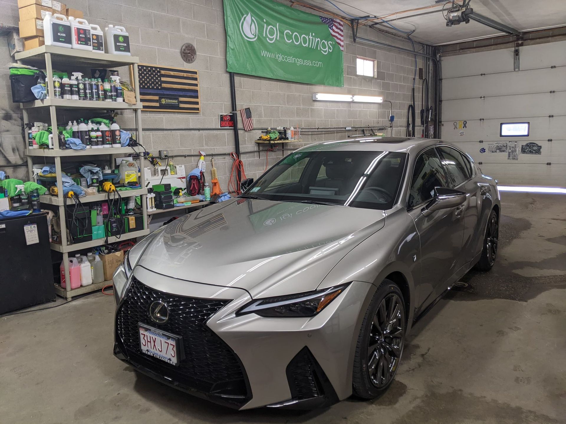 A silver Lexus sedan parked inside a workshop with a storage shelf filled with cleaning supplies in the background.