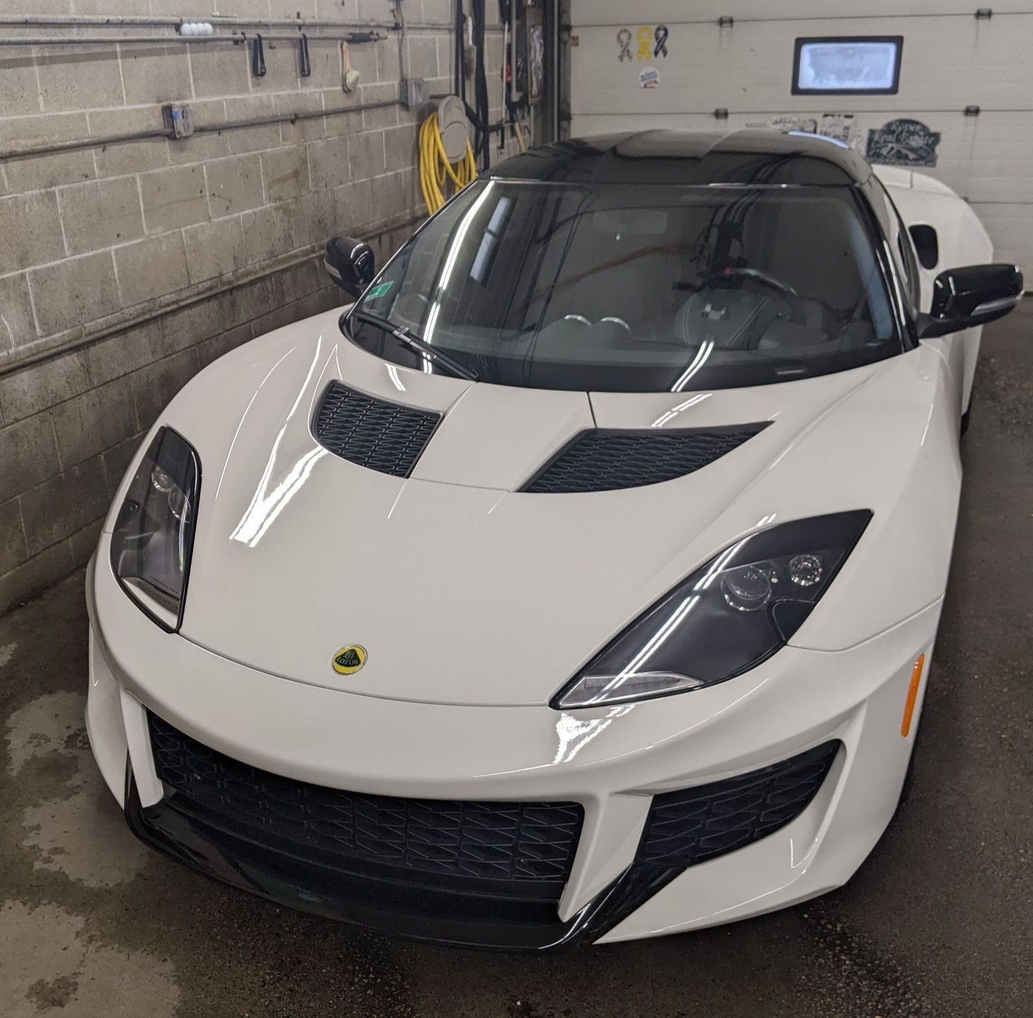 A white Lotus sports car with a black roof parked inside a garage.