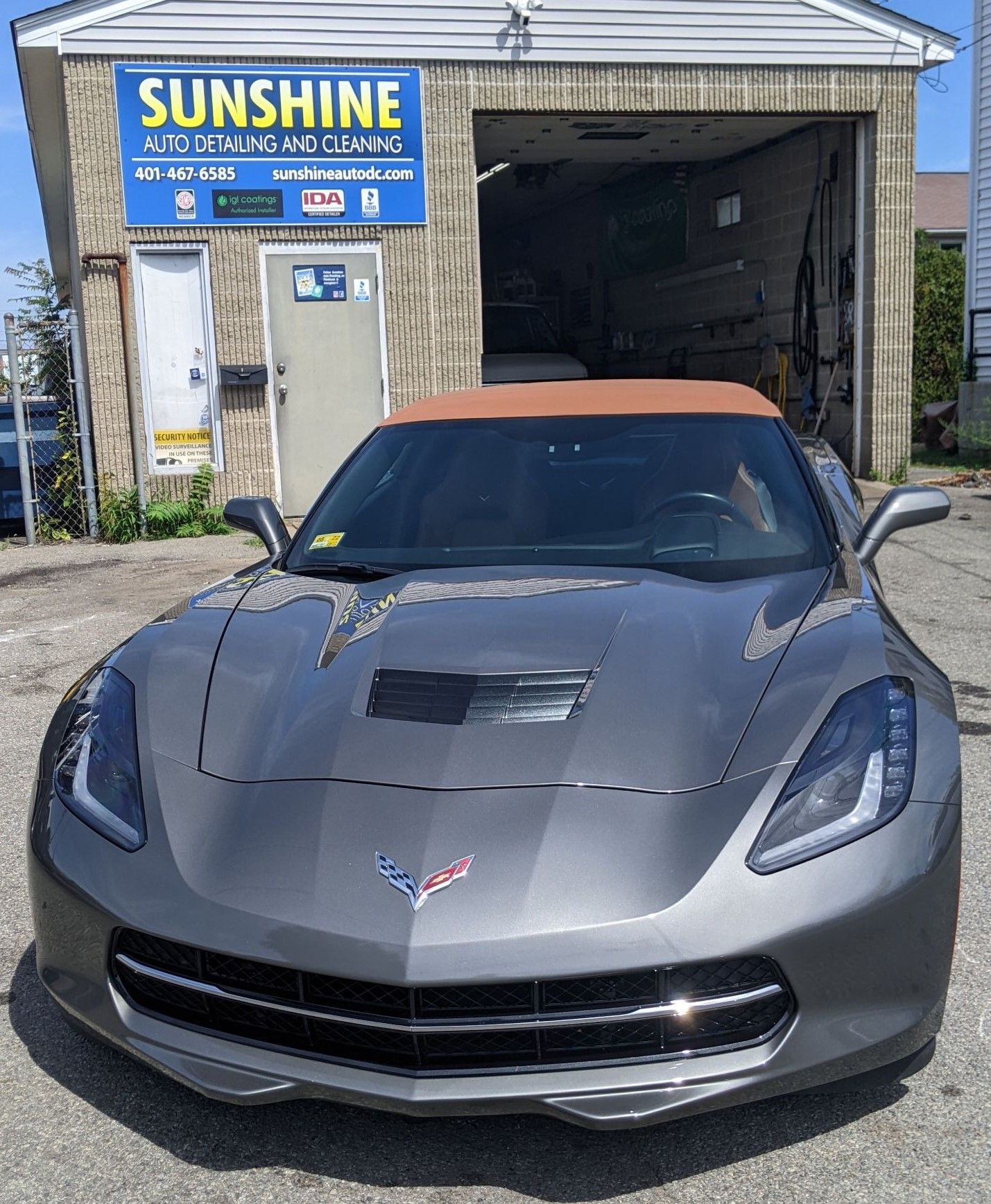 A gray Chevrolet Corvette convertible parked in front of the Sunshine Auto Detailing business.